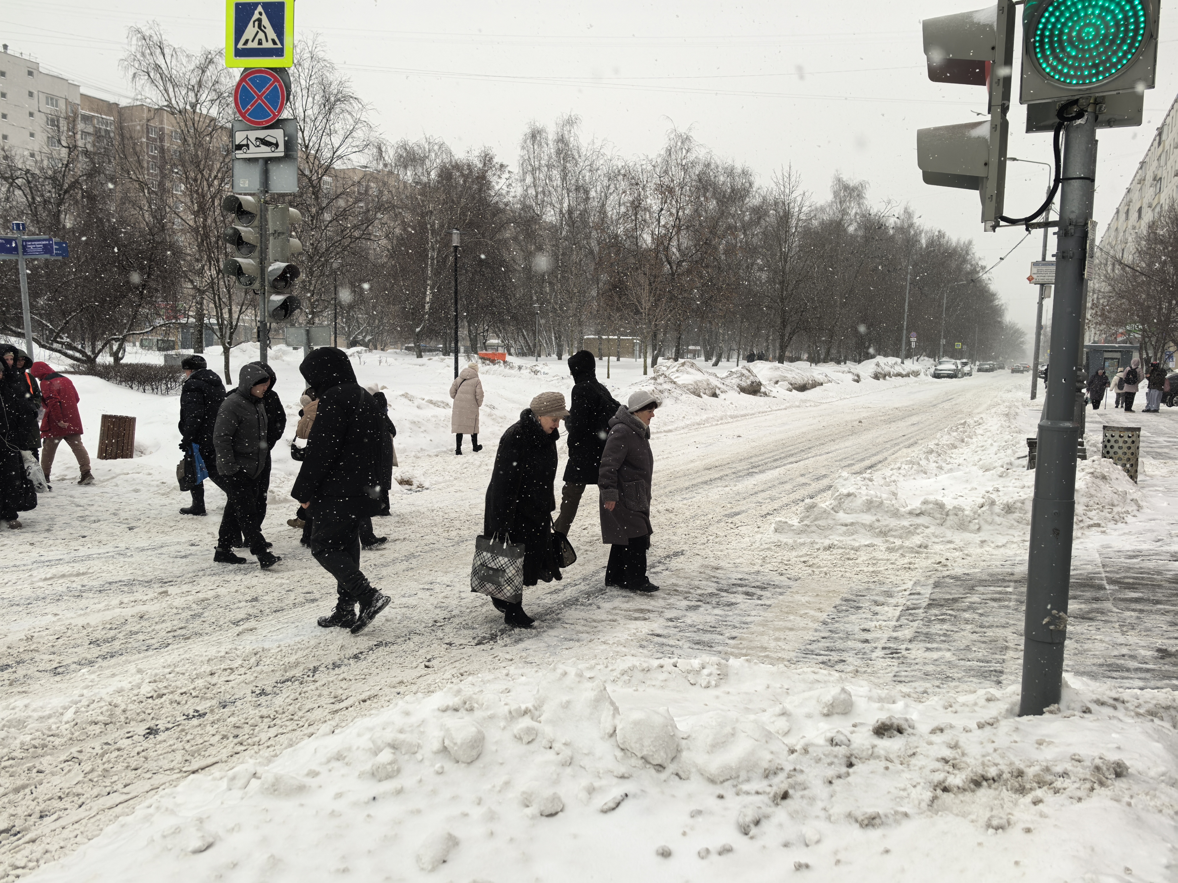 Городская улица с пешеходным переходом, оборудованным светофором. На улице зима, идет снег, покрытие дороги и тротуаров покрыто снегом и наледью.