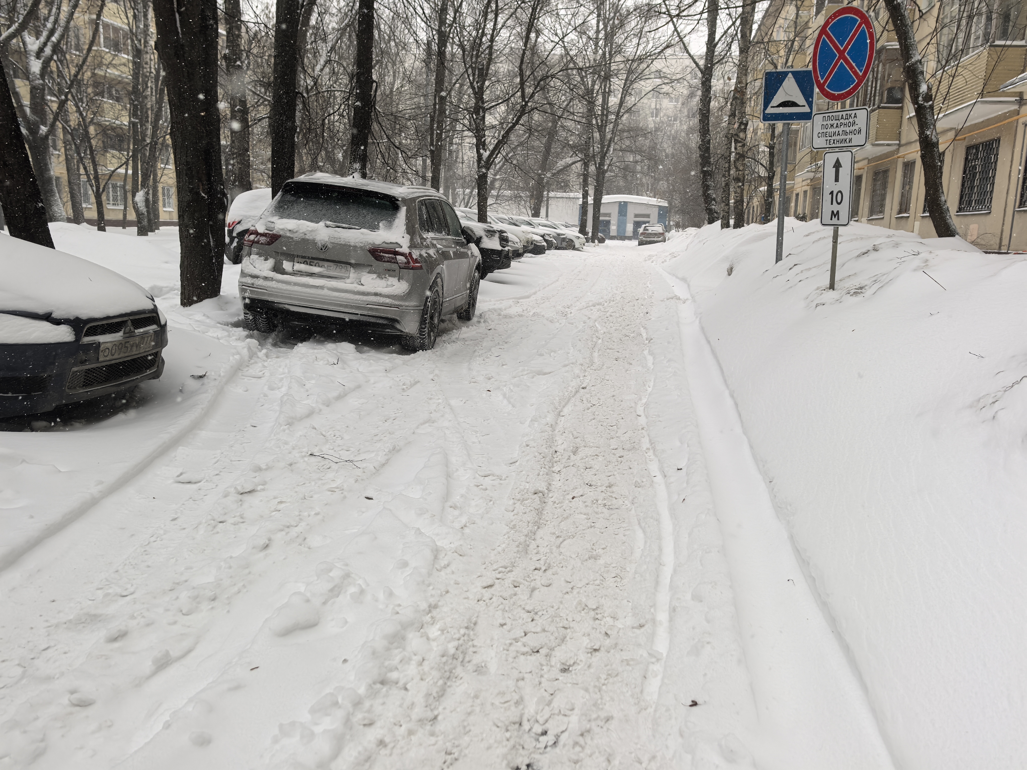 Дворовая территория, заснеженная проезжая часть с припаркованными автомобилями, отсутствуют пешеходные переходы и тротуары.