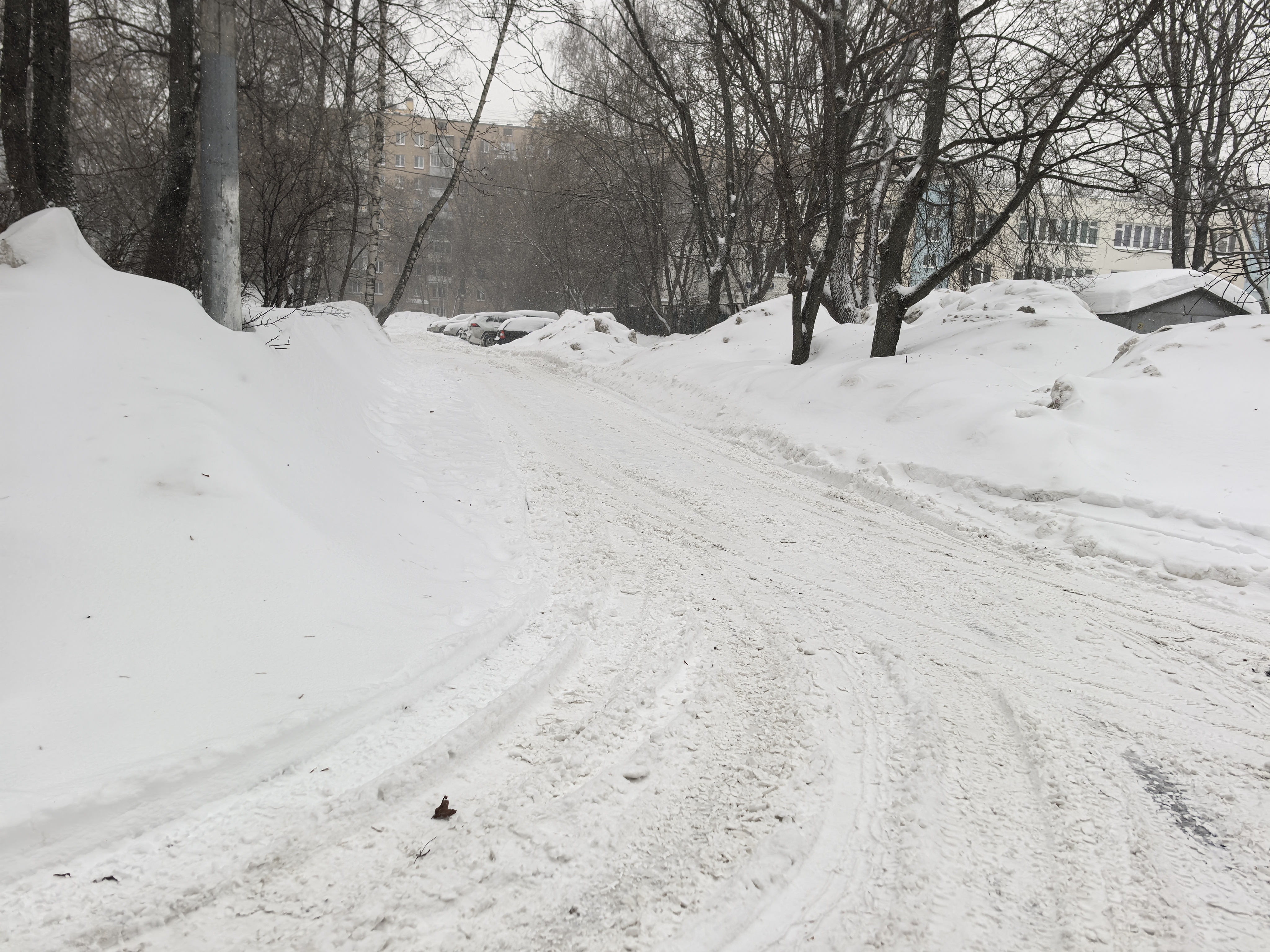 Дворовая территория, покрытая снегом, с припаркованными автомобилями и жилыми домами на заднем плане