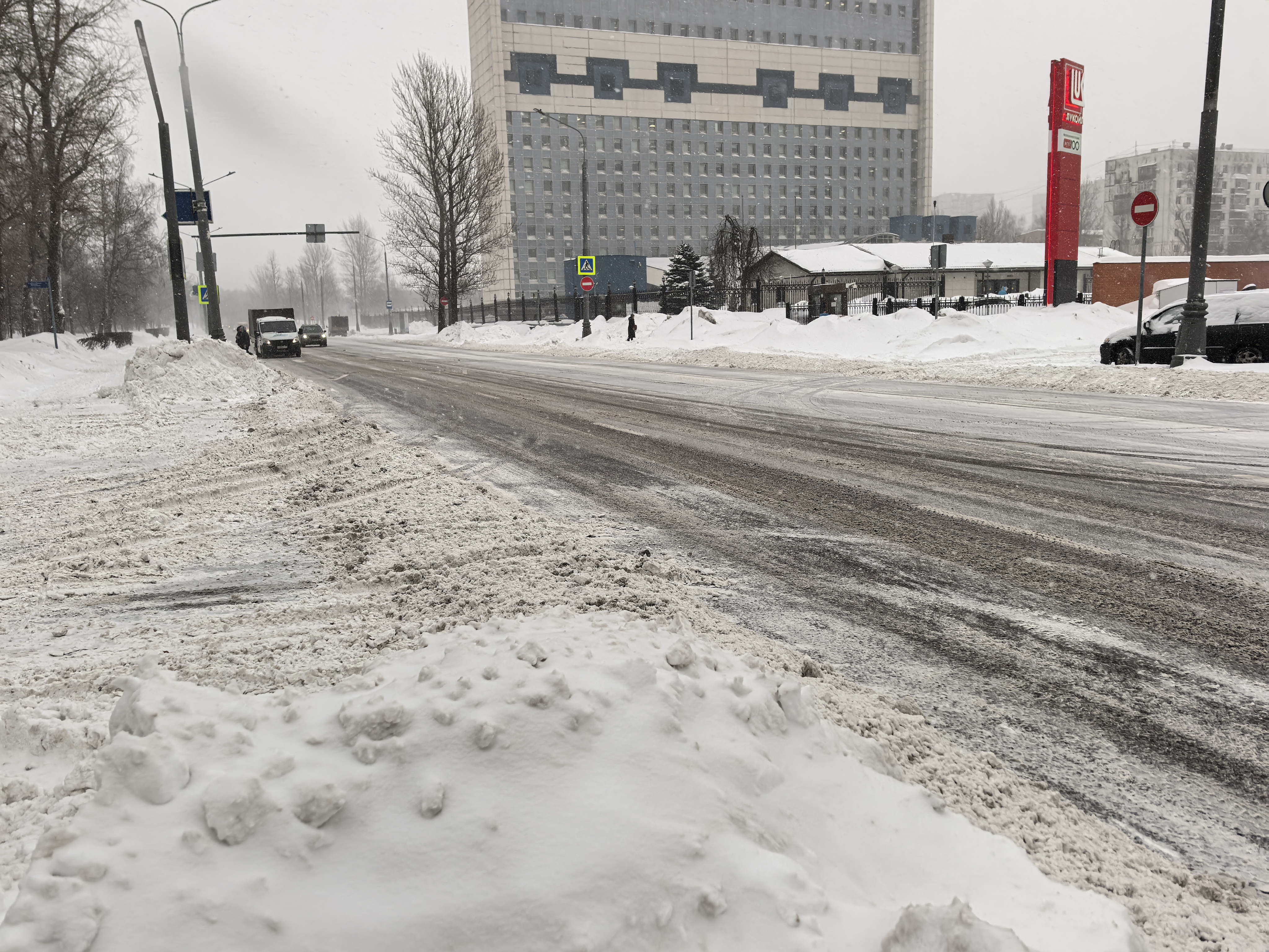 Широкая городская дорога с пешеходным переходом в зимних условиях, виден знак перехода и разметка, покрытая снегом.