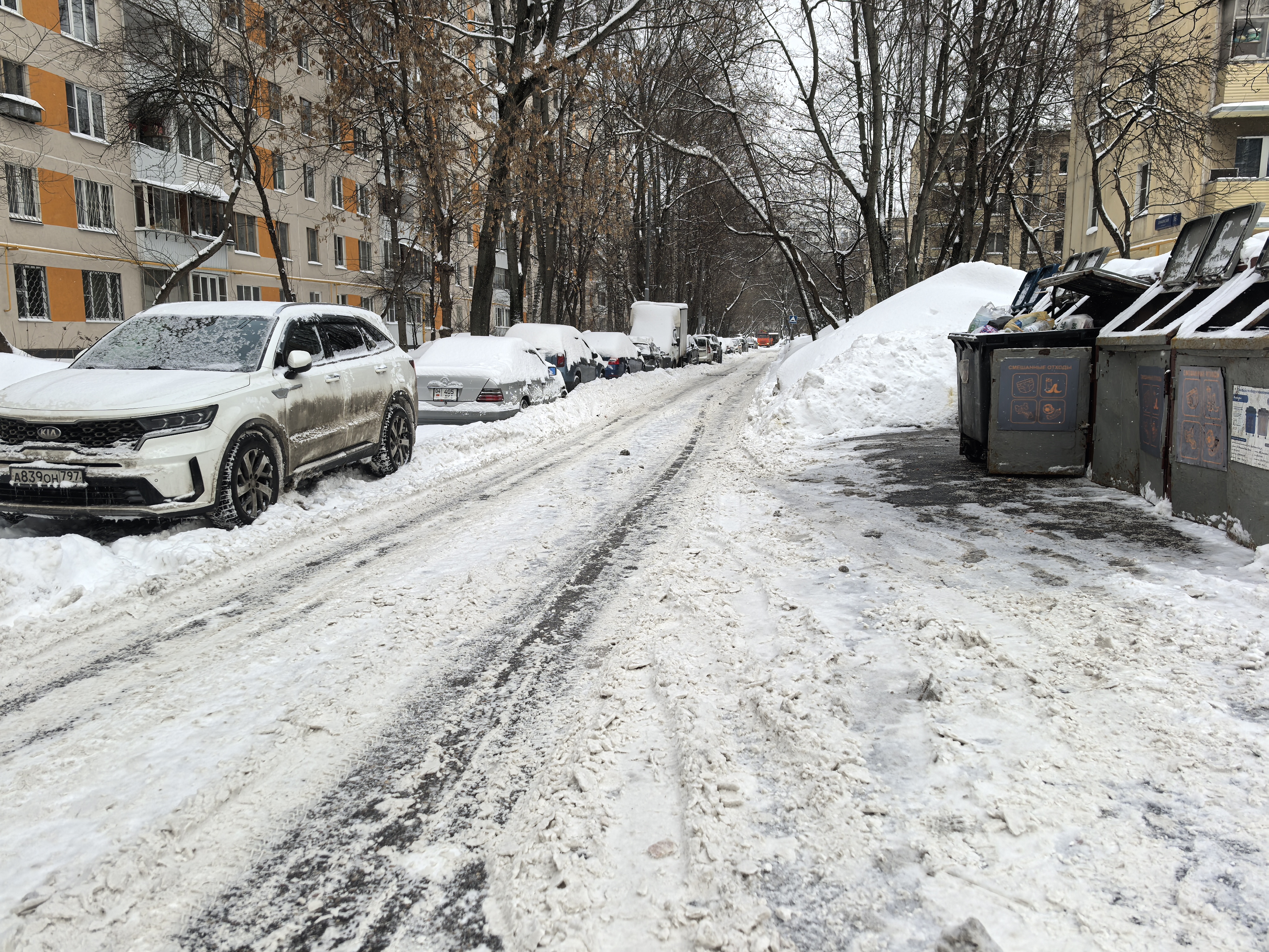 Дворовая территория между жилыми домами, заснеженная дорога, припаркованные автомобили, контейнеры для мусора