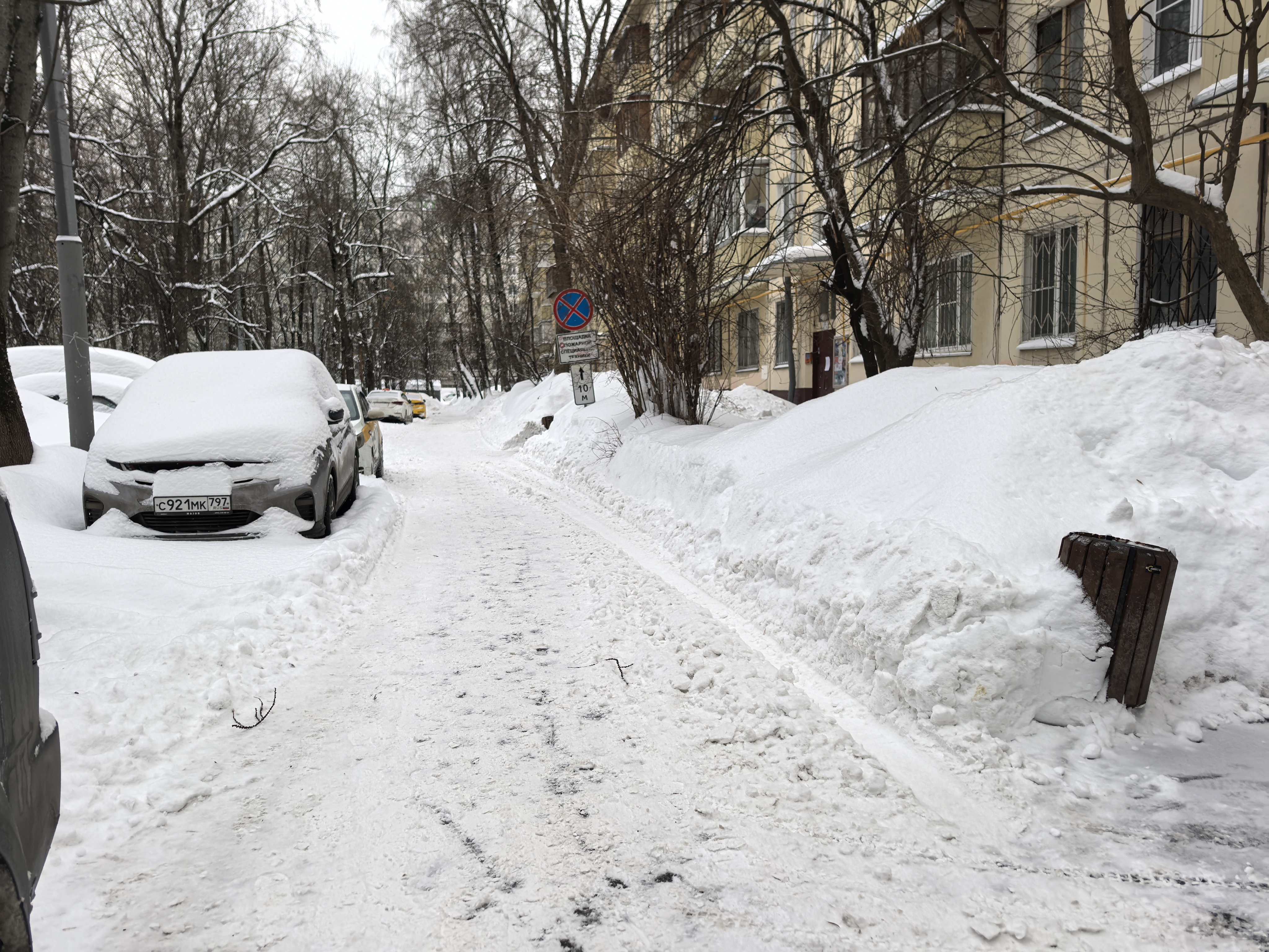 Дворовая территория, заснеженная дорога между жилыми домами, припаркованные автомобили, отсутствуют пешеходные переходы и тротуары в классическом понимании.