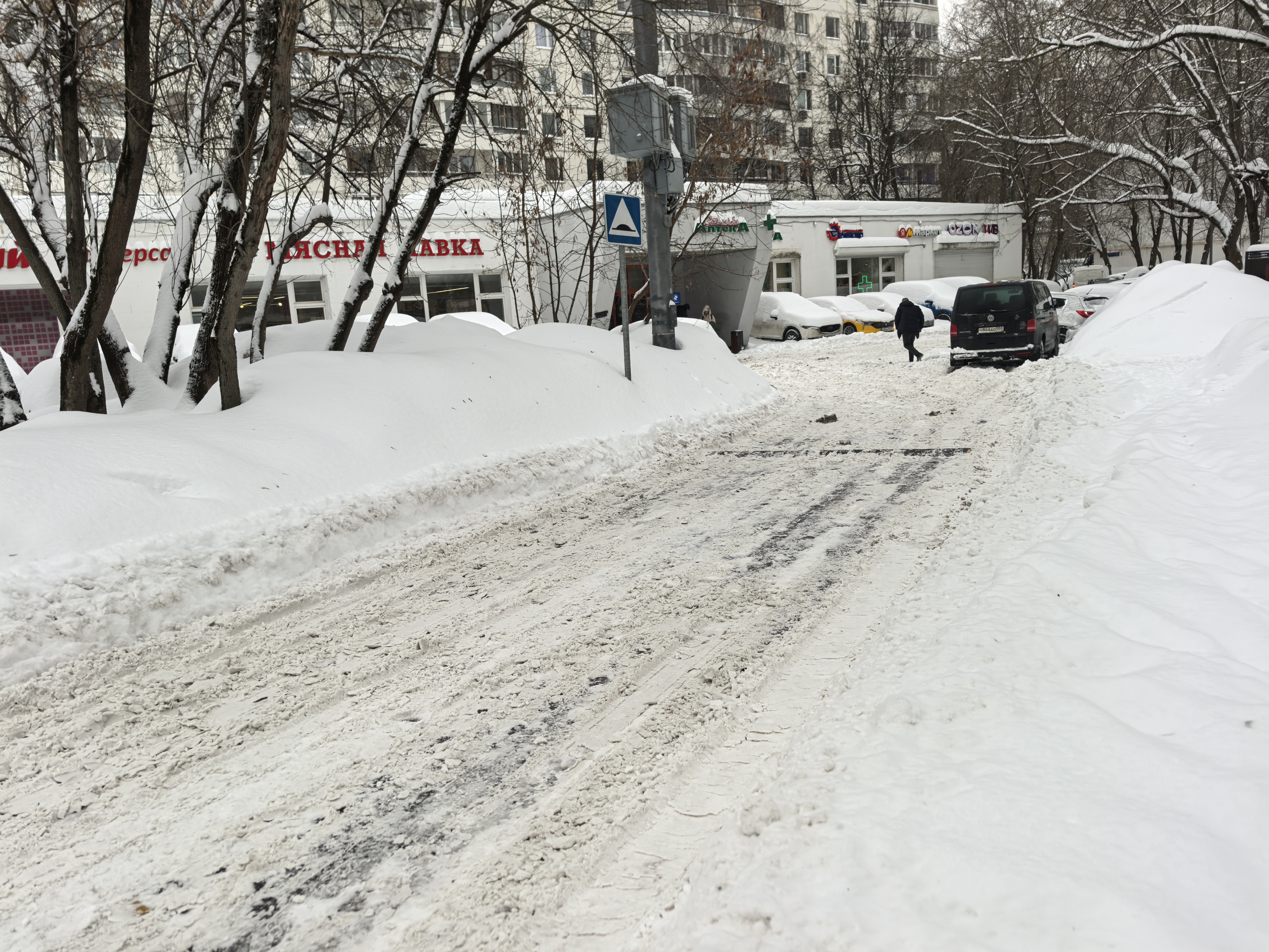 Дворовая территория или подъезд к магазинам, покрытая снегом. Видны припаркованные автомобили, жилой дом на заднем плане и дорожный знак «Неров原原原原原原原原原原原原原原原原原原原原原原原原原原原原原原原原原原原原原原原原原原原原原原原原原原原原原原原原原原原原原原原原原原原原原原原原原原原原原原原原原原原原原原原原原原原原原原原原原原原原原原原原原原原原原原原原