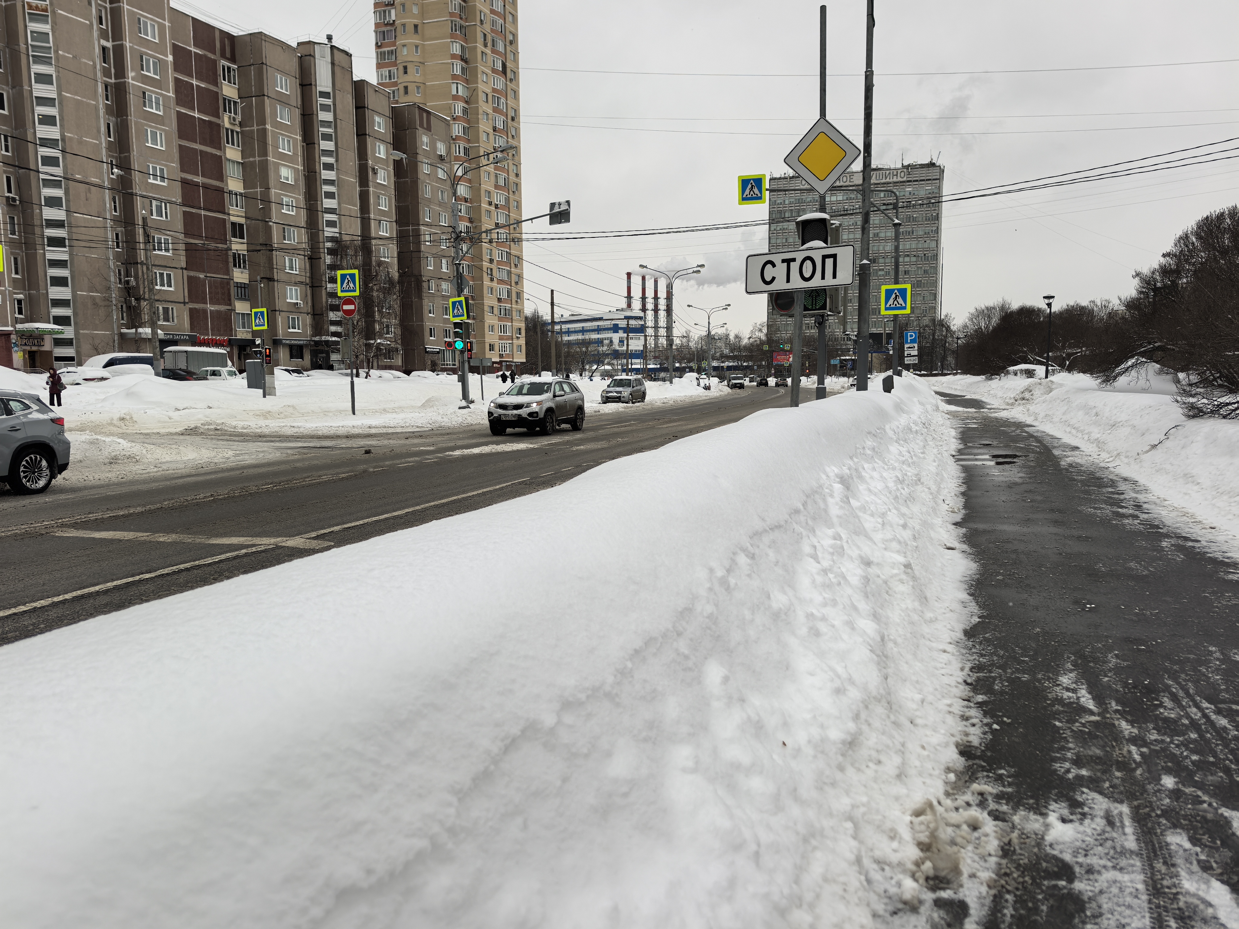Городская улица с пешеходным переходом, регулируемым светофором. Снежные заносы на обочинах и тротуарах.