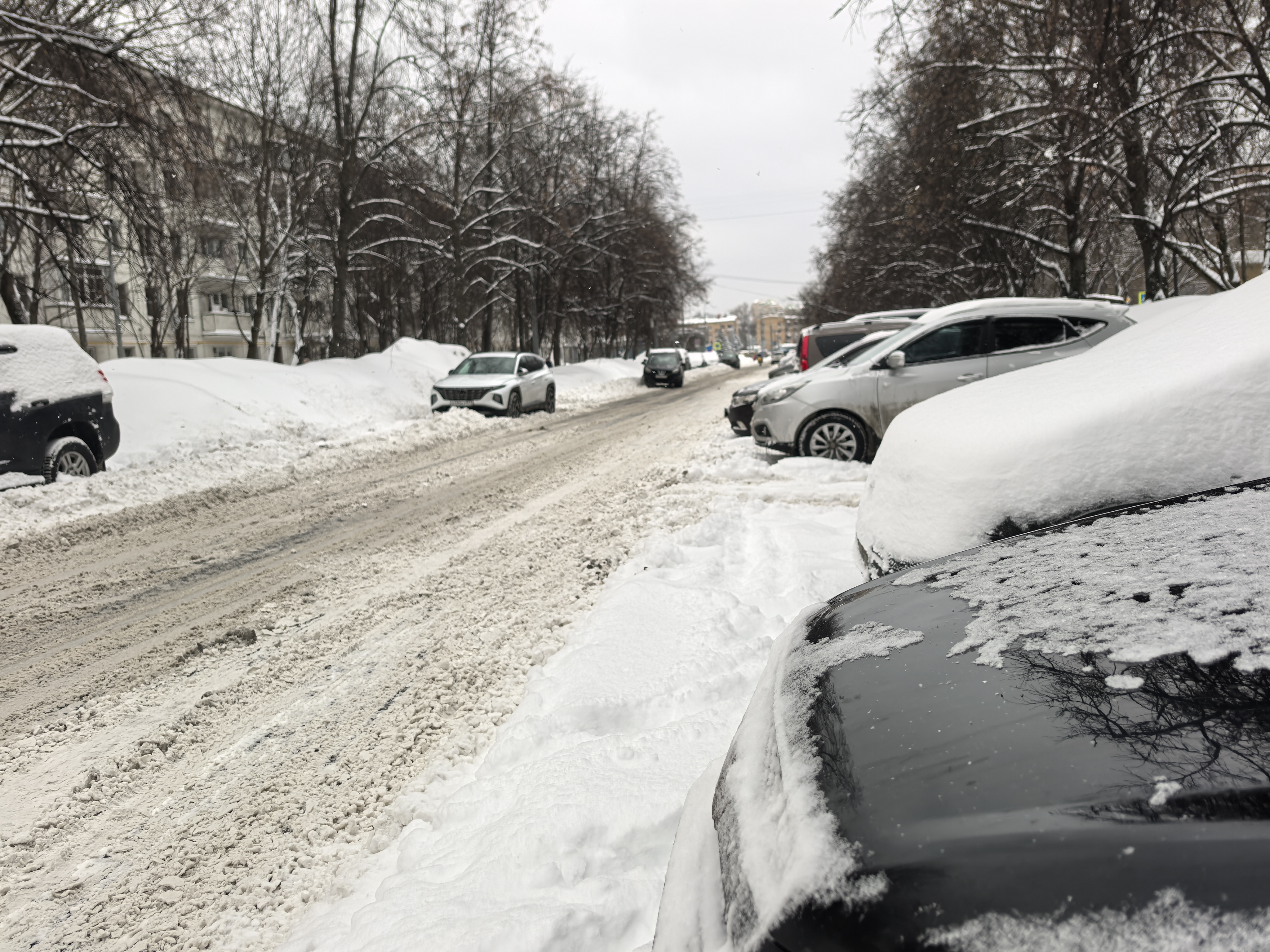 Участок городской улицы в зимний период, без пешеходного перехода. Дорога покрыта снегом и слякотью, тротуары полностью засыпаны снегом. Парковка автомобилей происходит непосредственно у проезжей части.