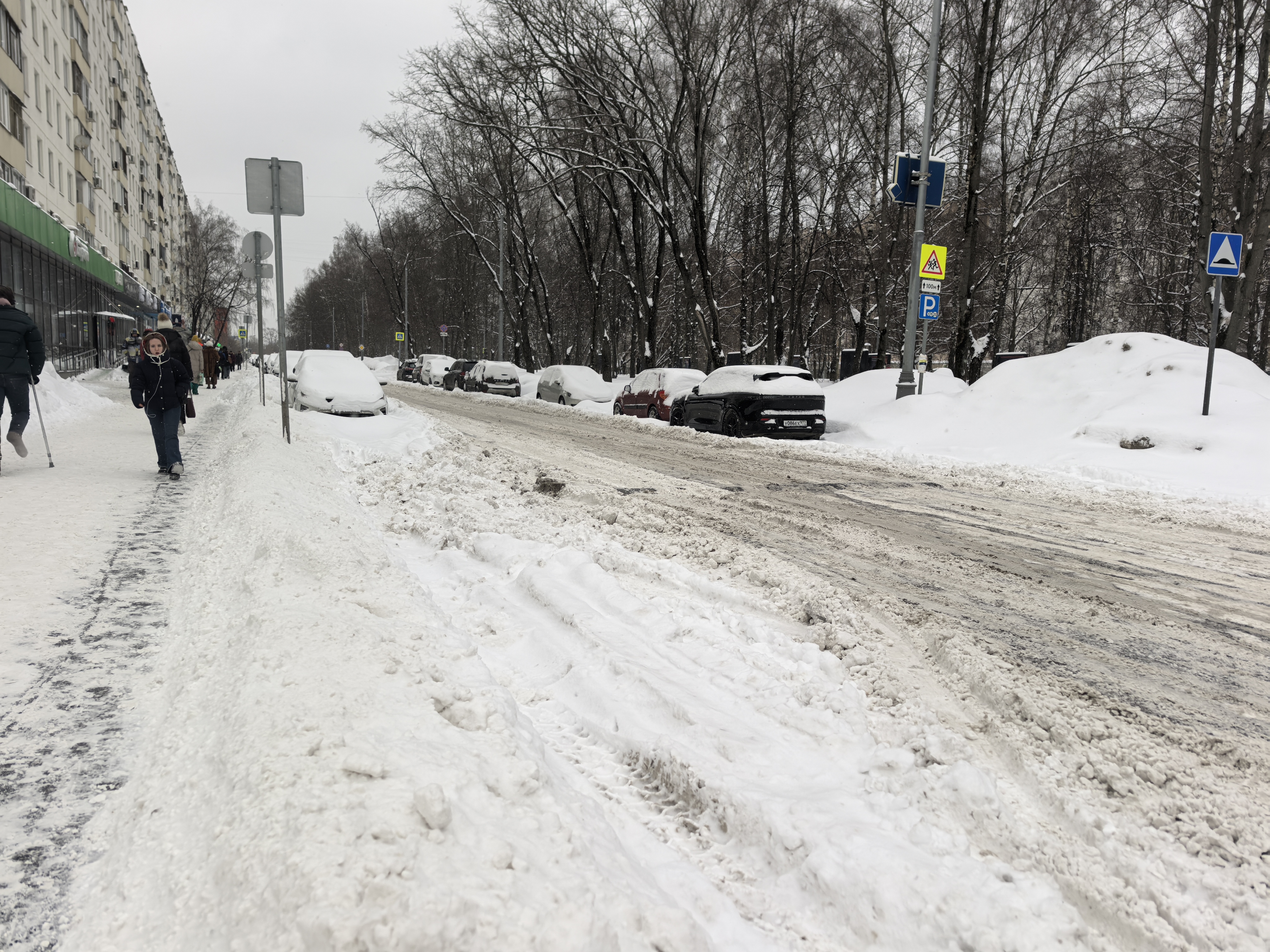 Городская улица с пешеходным переходом (зебра), покрытая снегом и грязью. Видны припаркованные автомобили, закрывающие обзор.