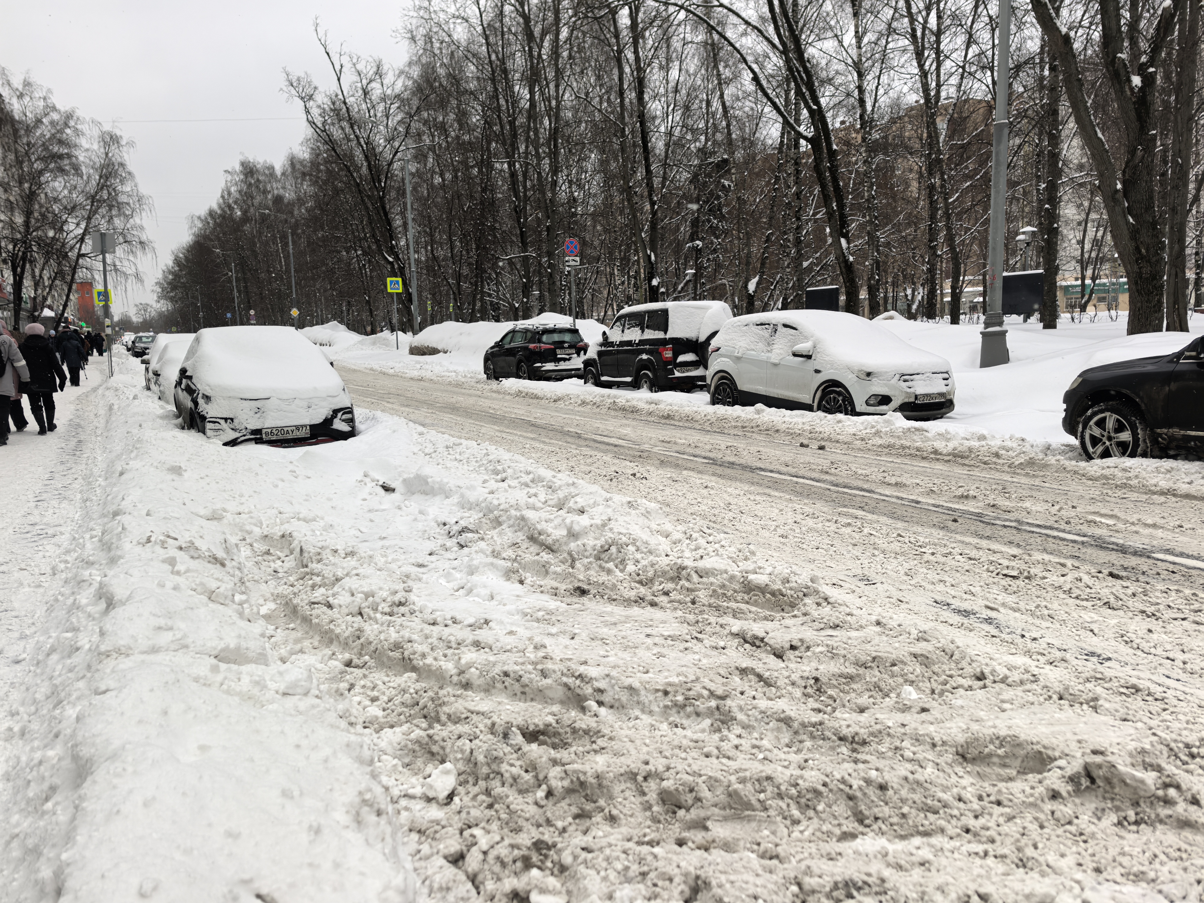 Проезжая часть без обустроенного пешеходного перехода. Зимний период, на дороге снег и слякоть. Тротуары частично засыпаны снегом, припаркованные автомобили стоят на обочине и на тротуаре.