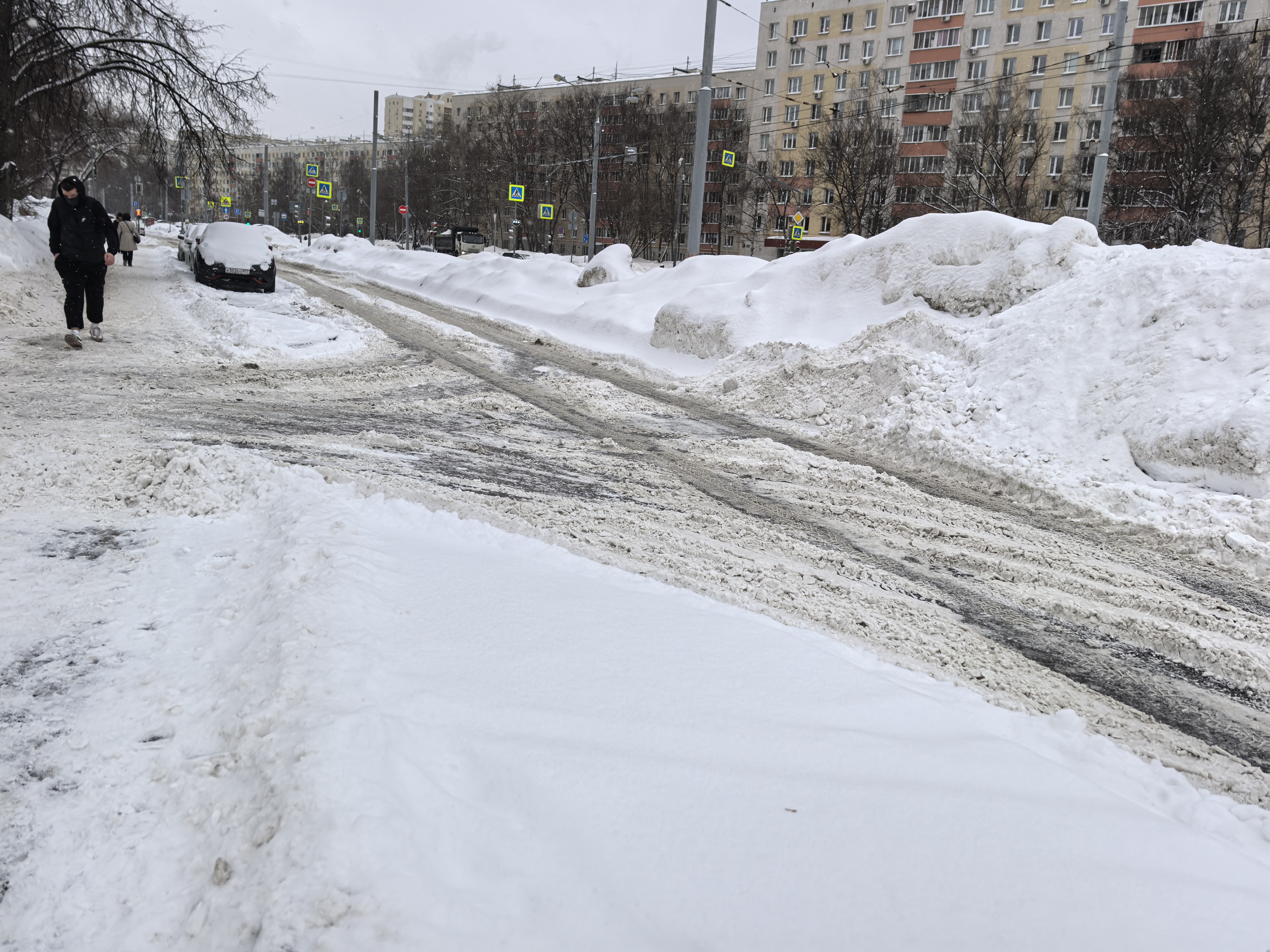 Городская проезжая часть в зимних условиях, оборудованная тротуаром. Пешеходный переход в непосредственной близости виден, но на данном участке его разметка не просматривается.
