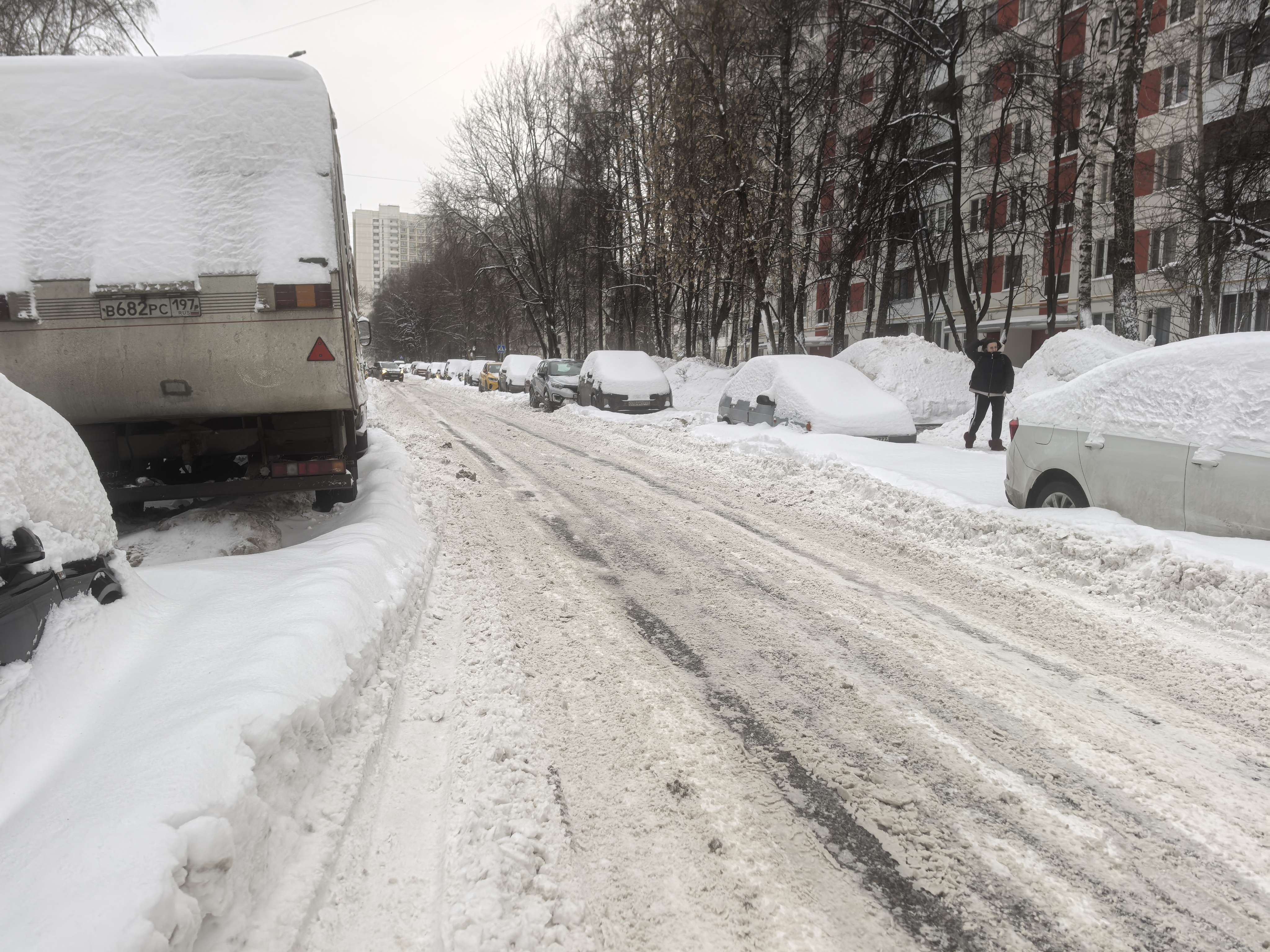 Участок проезжей части с припаркованными автомобилями, покрытый снегом и слякотью. Пешеходный переход отсутствует, тротуары засыпаны снегом.
