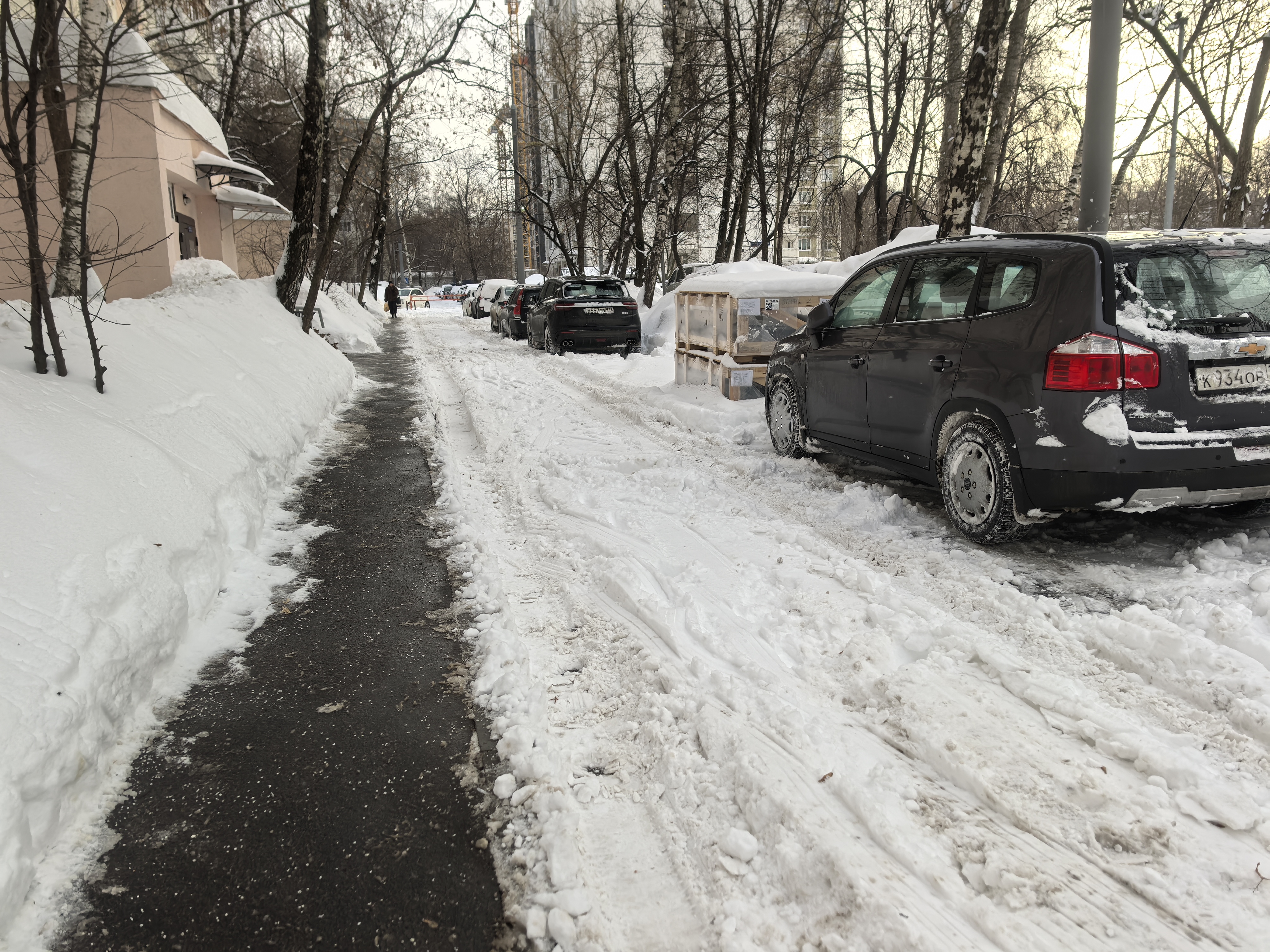 Участок дороги без пешеходного перехода. Слева виден тротуар, очищенный от снега, справа — проезжая часть, покрытая снегом и льдом, с припаркованными автомобилями.