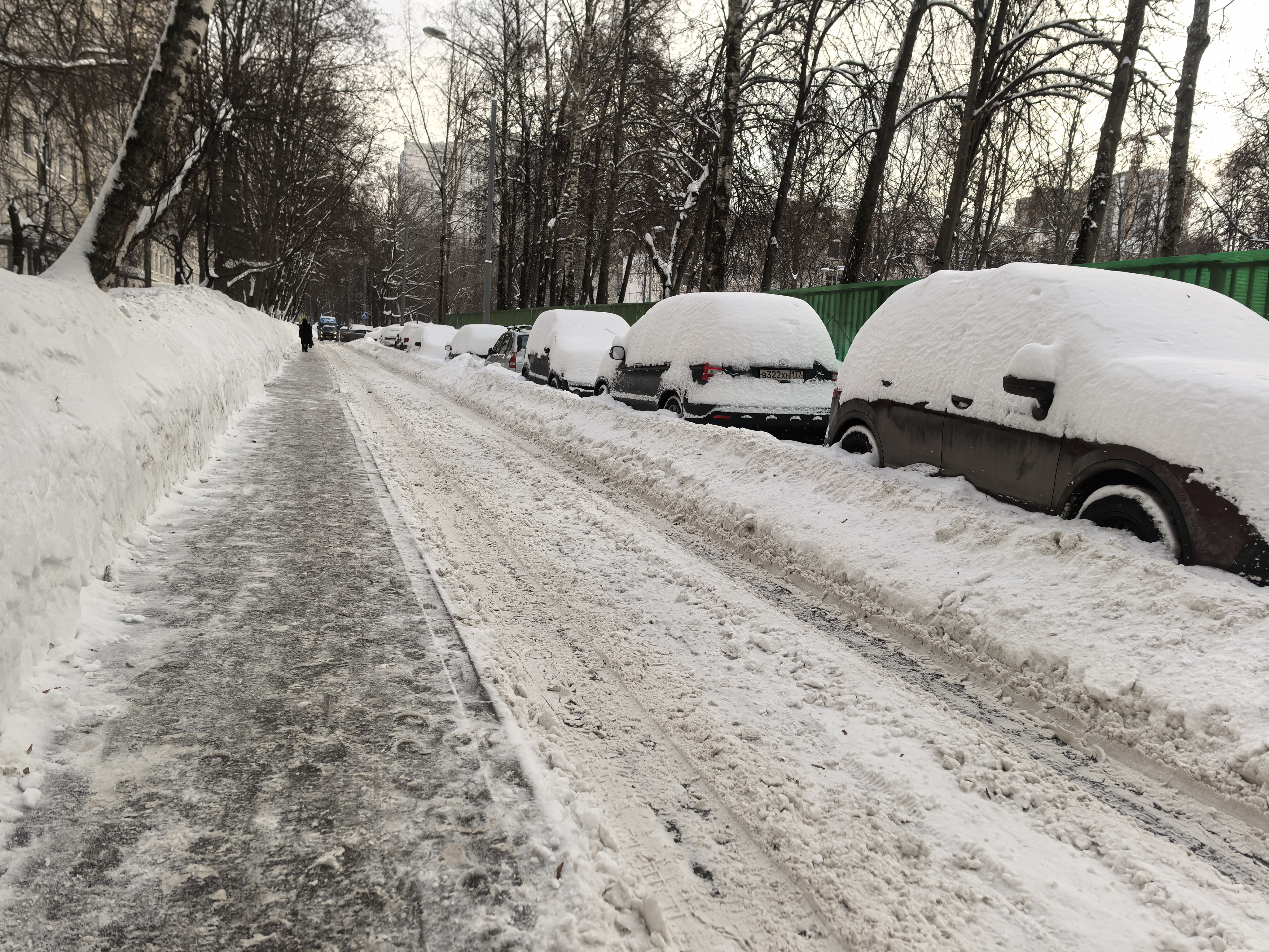 Участок проезжей части без пешеходного перехода, покрытый снегом и льдом. Справа припаркованы автомобили, слева — высокий снежный вал.