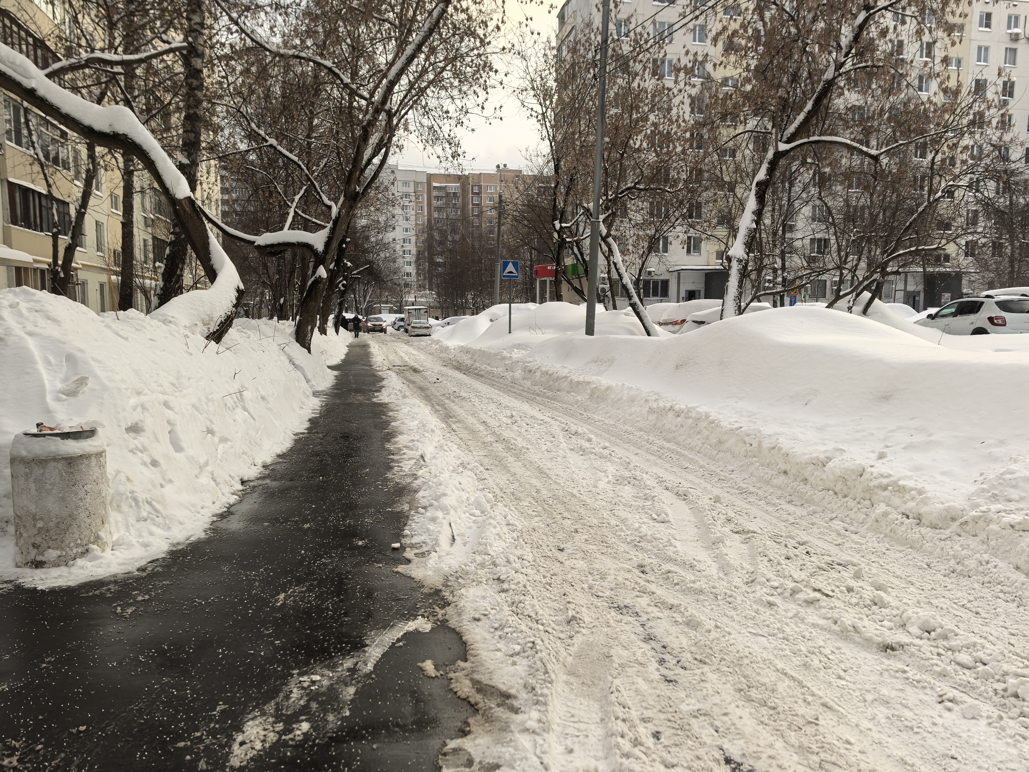 Участок дороги в жилом районе с узким пешеходным тротуаром, покрытым снегом, и проезжей частью, очищенной от снега, но имеющей снежную кашу. Пешеходный переход отсутствует.
