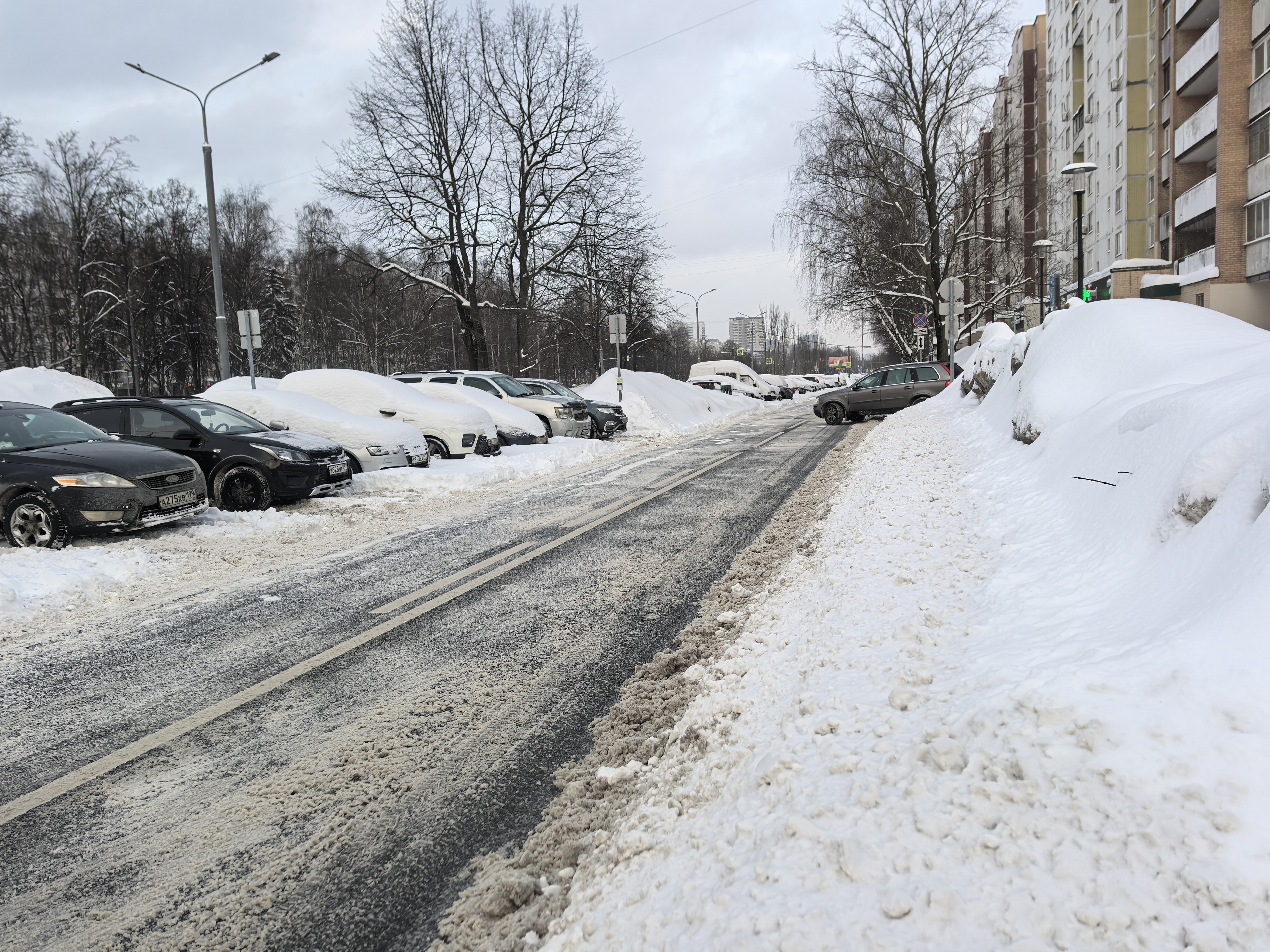 Участок проезжей части без пешеходного перехода, с припаркованными автомобилями и большими сугробами, ограничивающими обзор и проходимость.