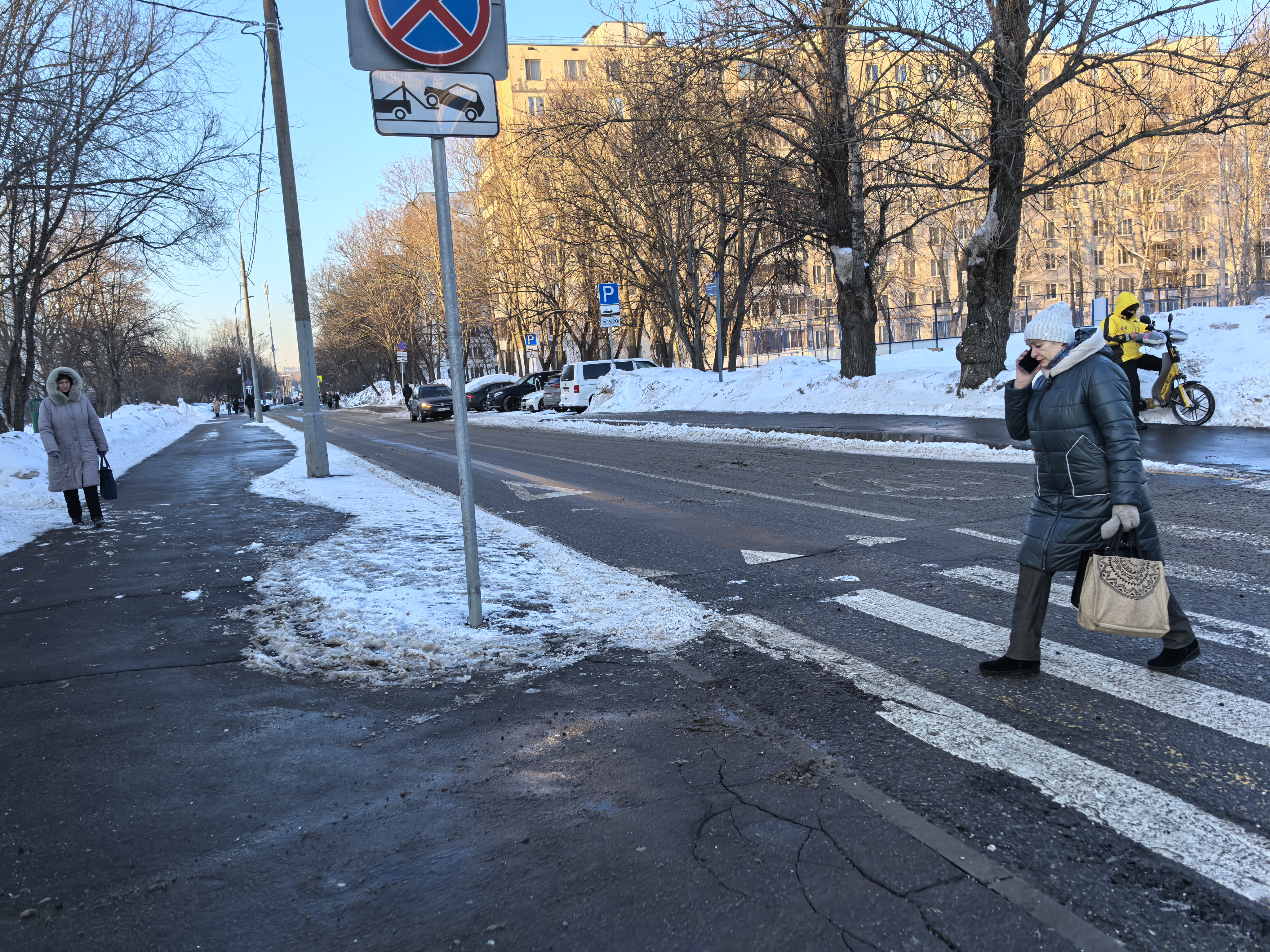Городская улица с пешеходным переходом, тротуаром и припаркованными автомобилями на обочине.