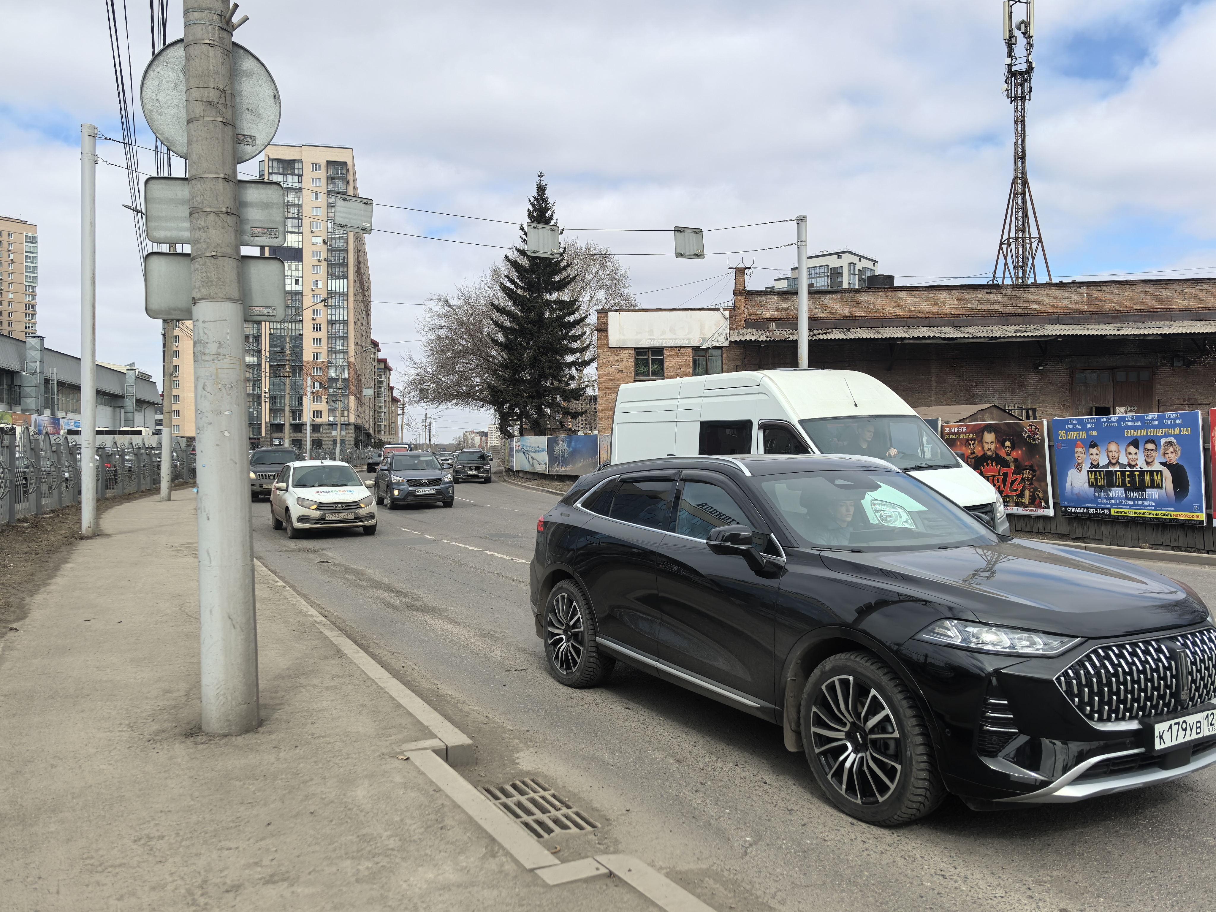 Городская улица с проезжей частью и тротуаром, пешеходный переход в кадре отсутствует. Видны движущиеся автомобили и припаркованный фургон.