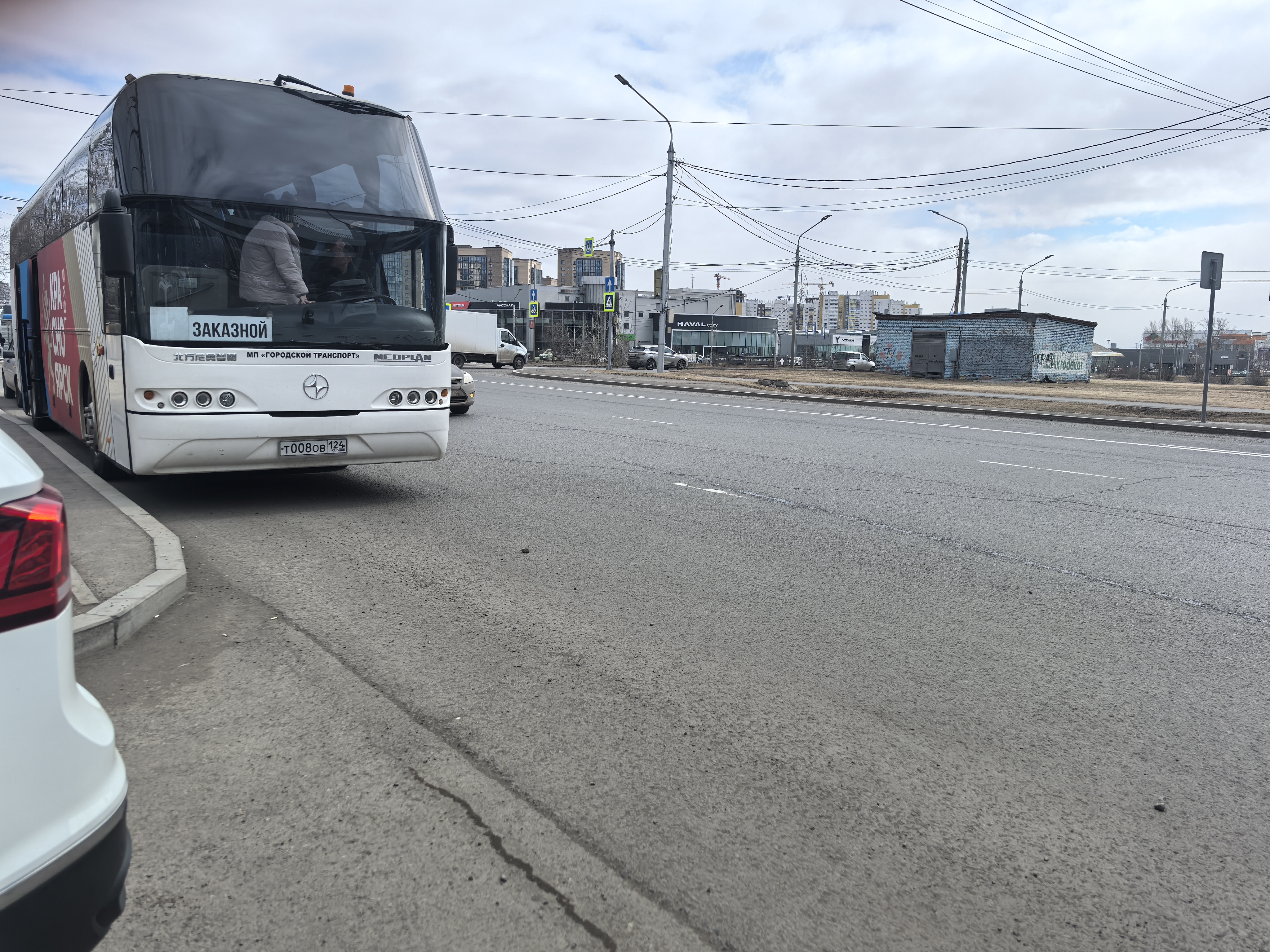 Широкая городская проезжая часть без видимого пешеходного перехода в кадре. На обочине стоит большой автобус, на тротуаре и газоне снега нет, видимость хорошая.