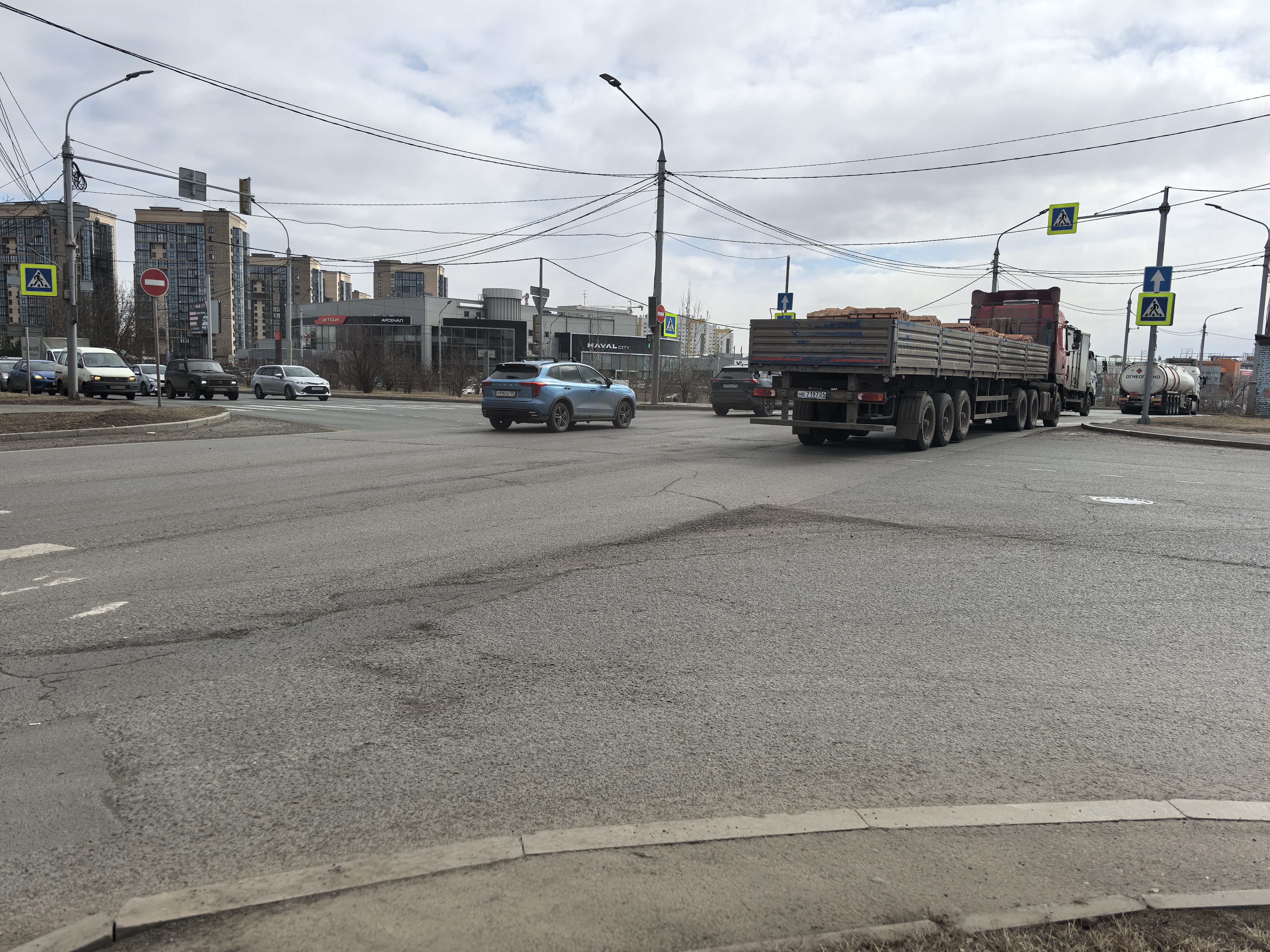 Перекресток с пешеходным переходом, регулируемым светофором, с интенсивным движением грузового и легкового транспорта.