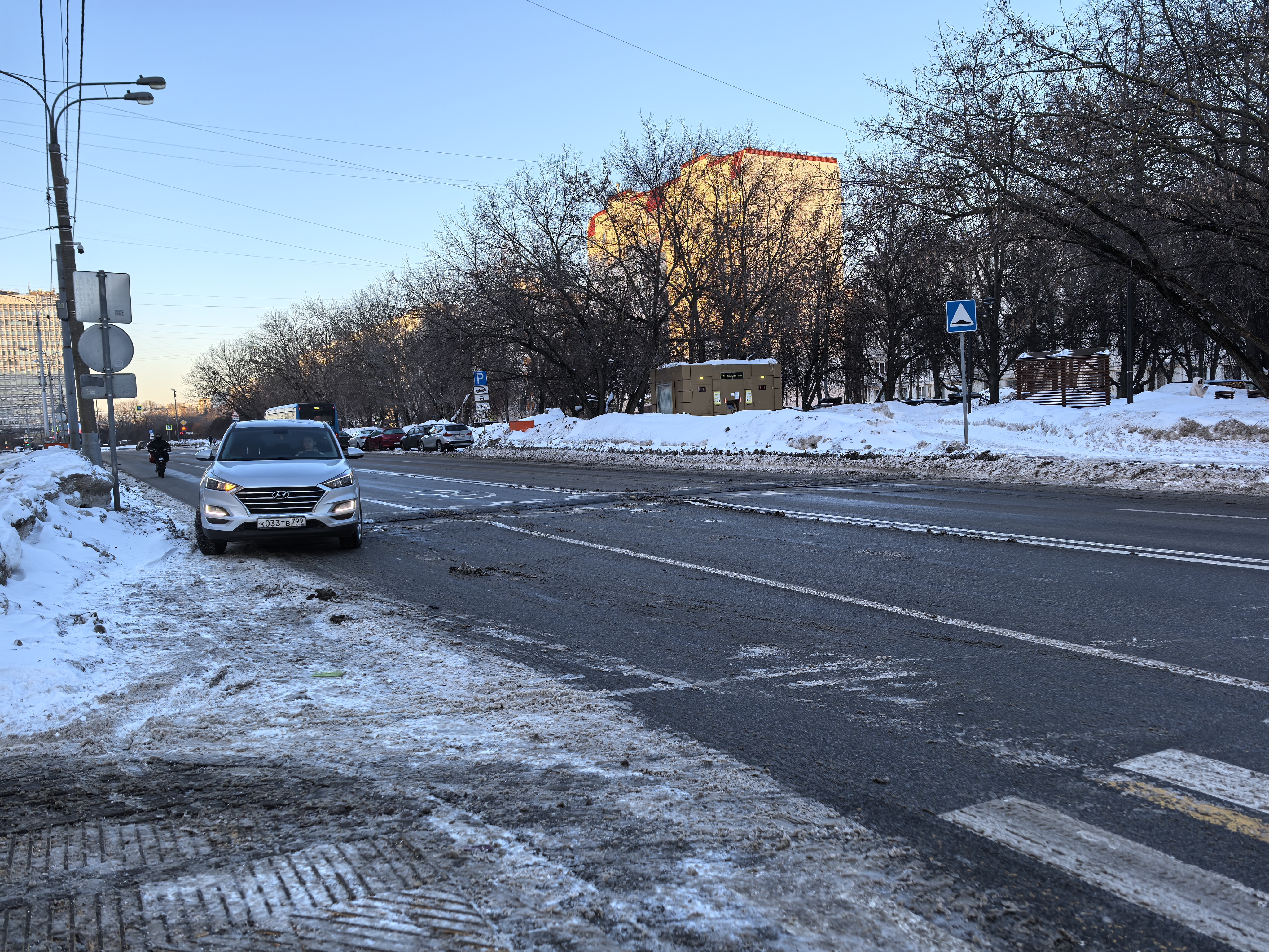 Городская проезжая часть с пешеходным переходом, зимний период, видны следы снега и грязи на обочинах и проезжей части.