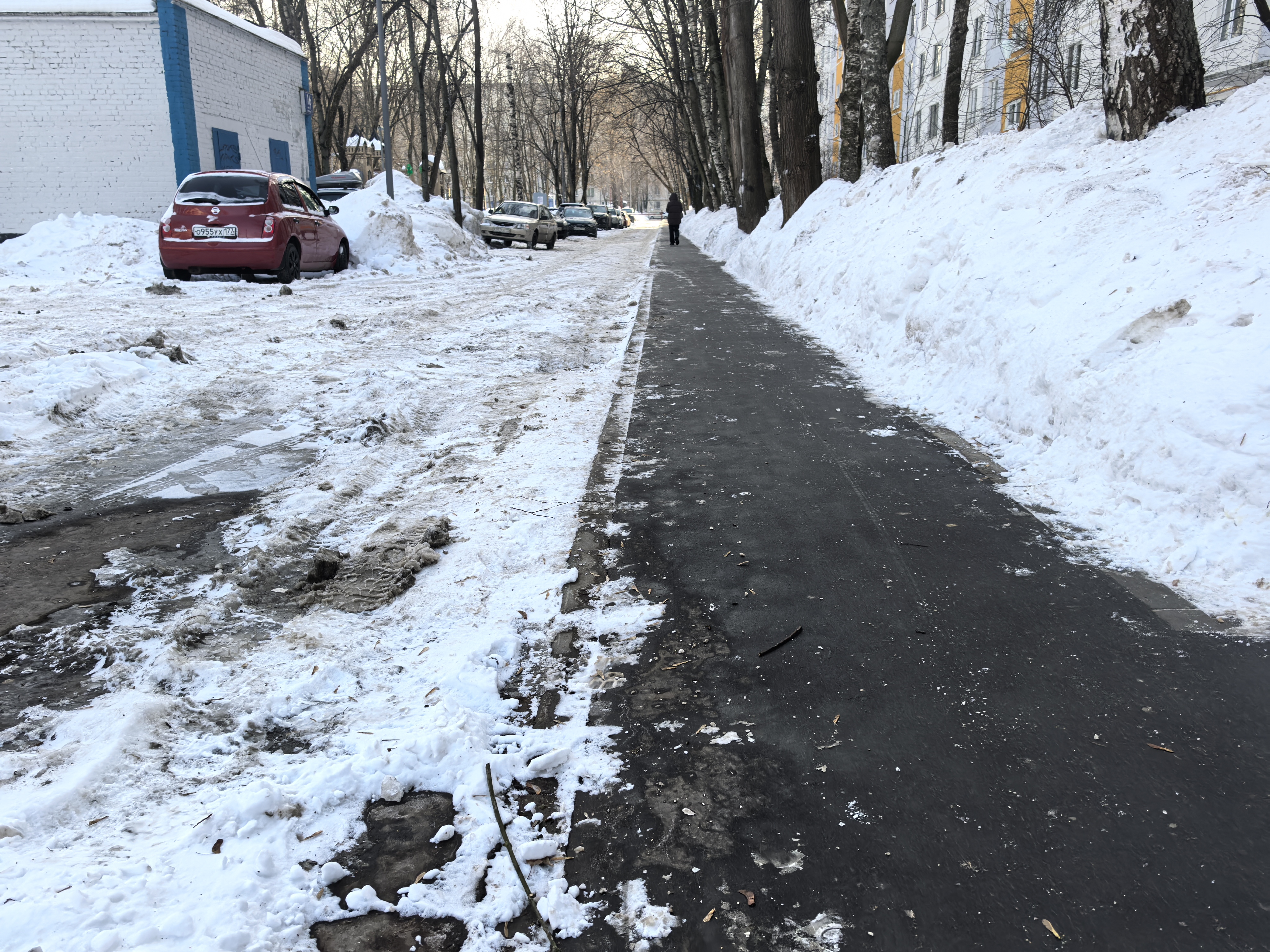 Участок проезжей части без пешеходного перехода, с тротуаром, покрытым снегом и льдом. Видны припаркованные автомобили, ограничивающие обзор.