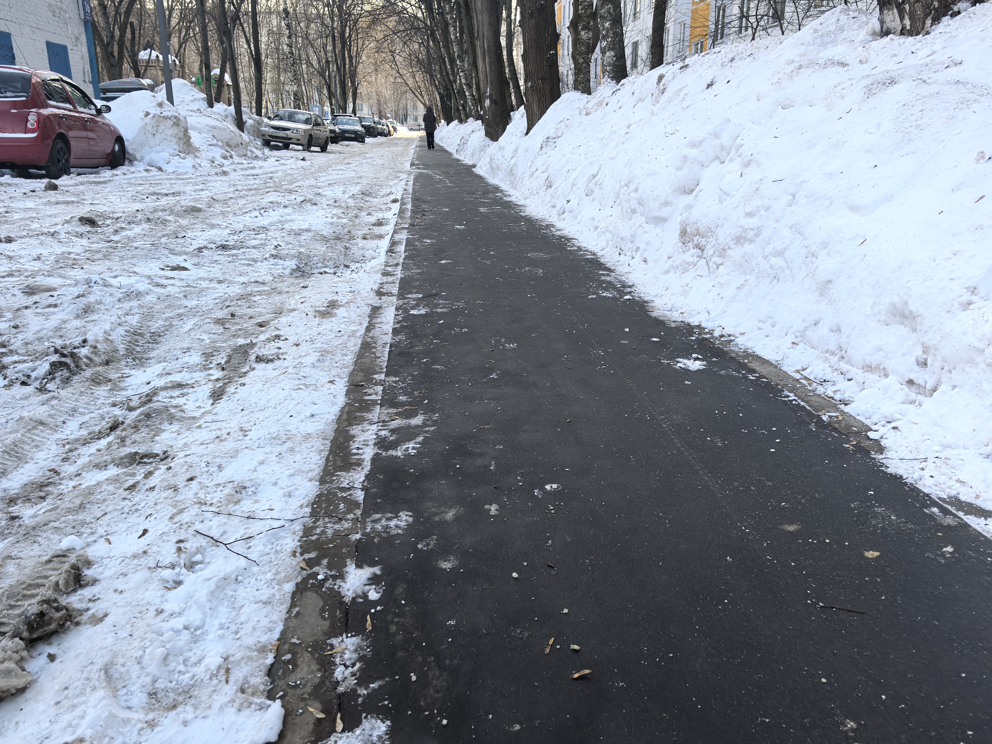 Участок дороги с тротуаром, но без пешеходного перехода. Тротуар чистый, проезжая часть покрыта снегом и грязью, припаркованы автомобили.