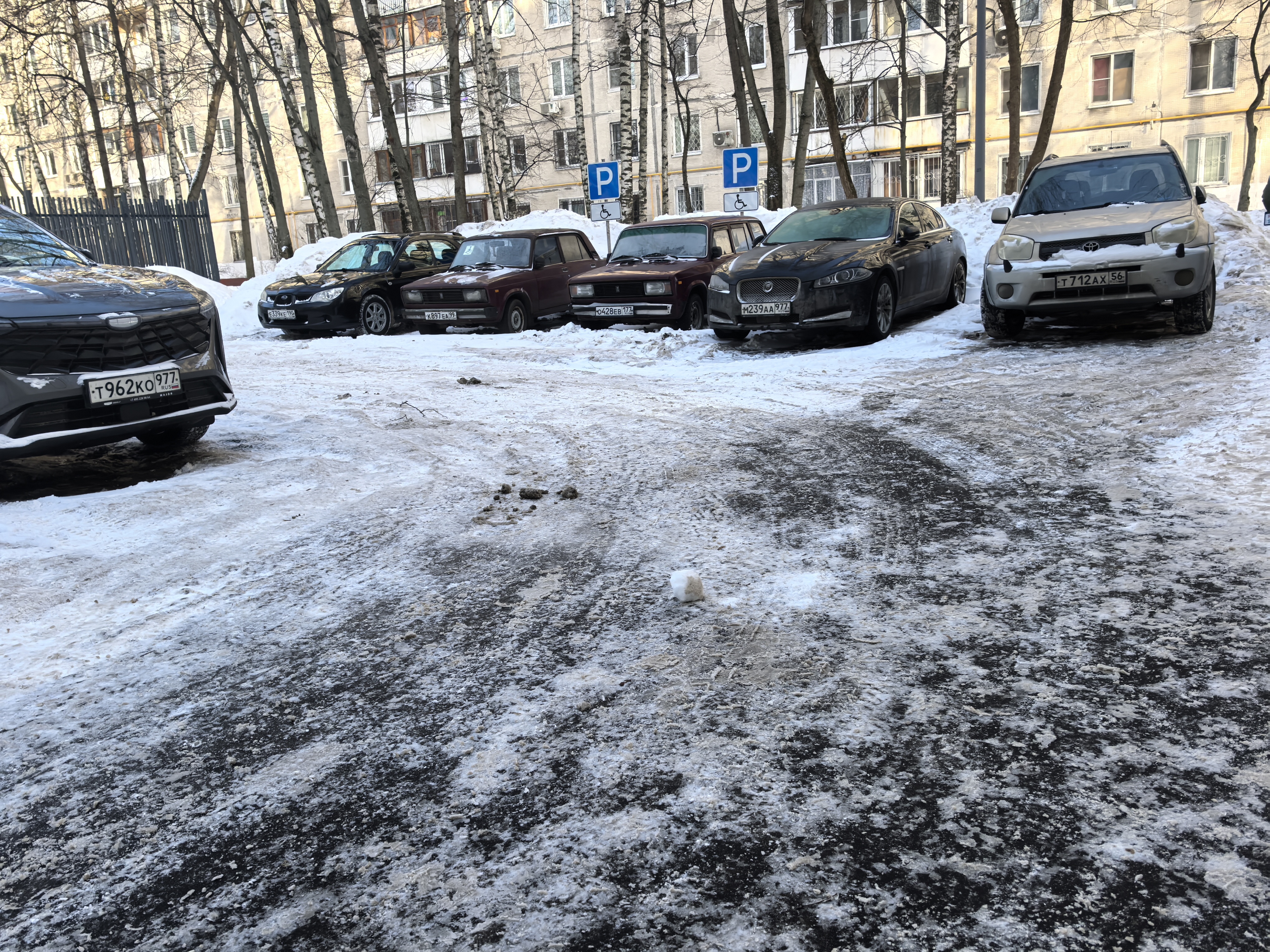 Дворовая территория с парковкой у жилого дома, покрытая снегом и льдом