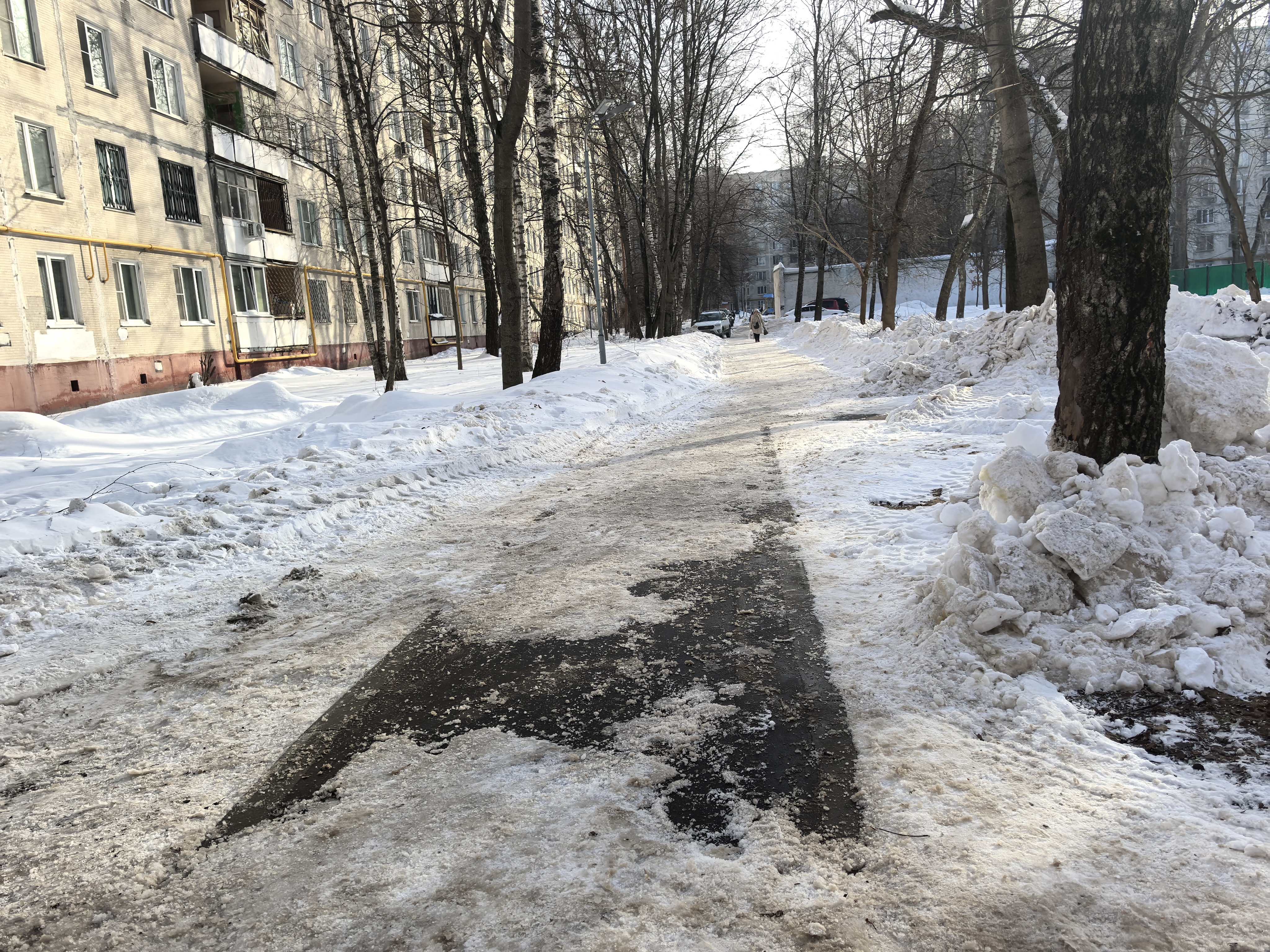 Дворовая территория между жилыми домами, покрытая снегом и льдом, с припаркованными автомобилями вдали