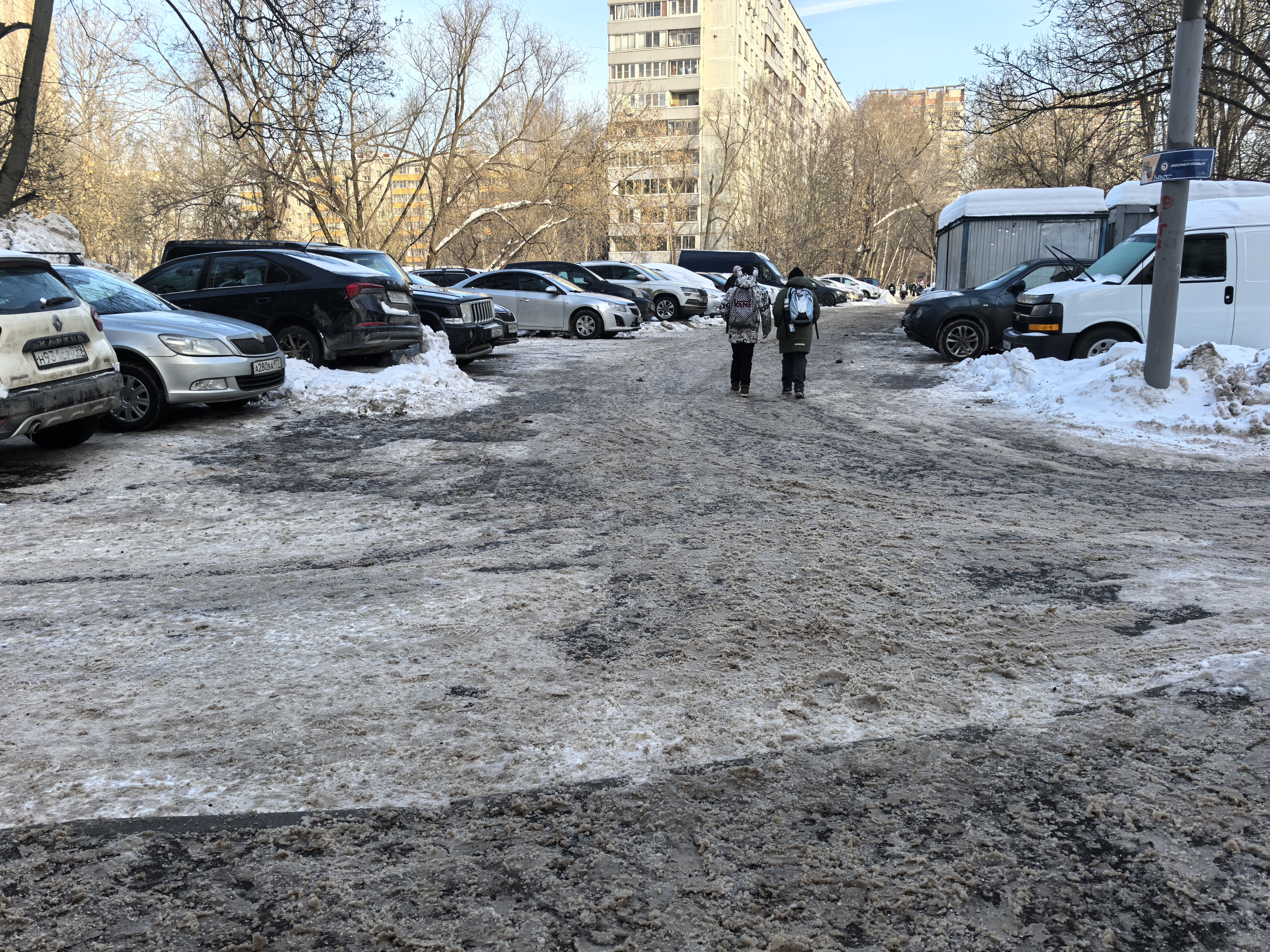 Дворовая территория с парковкой между жилыми домами, покрытая снегом и наледью.