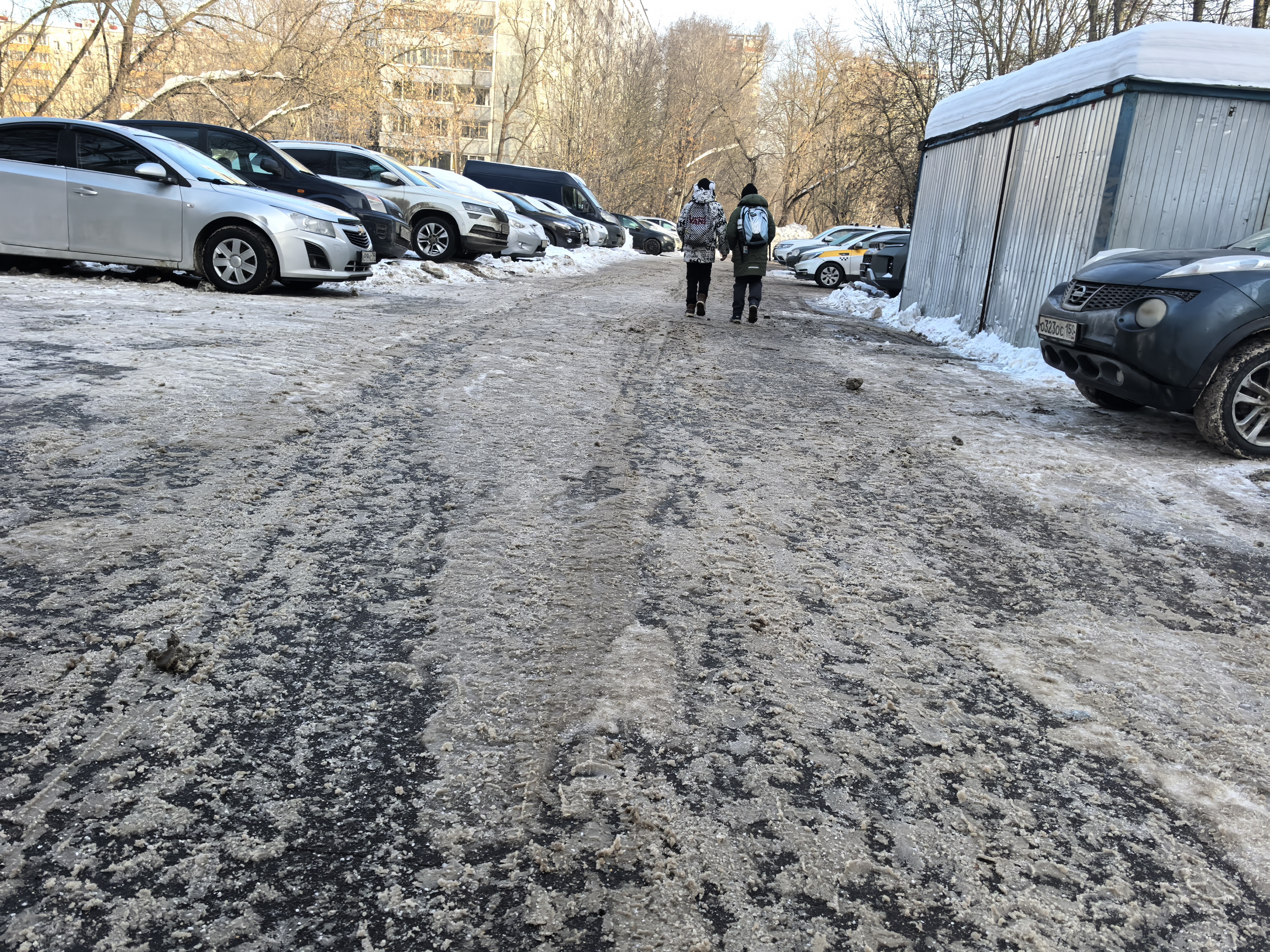 Дворовая территория с парковкой автомобилей и пешеходами, покрытая снегом и льдом.