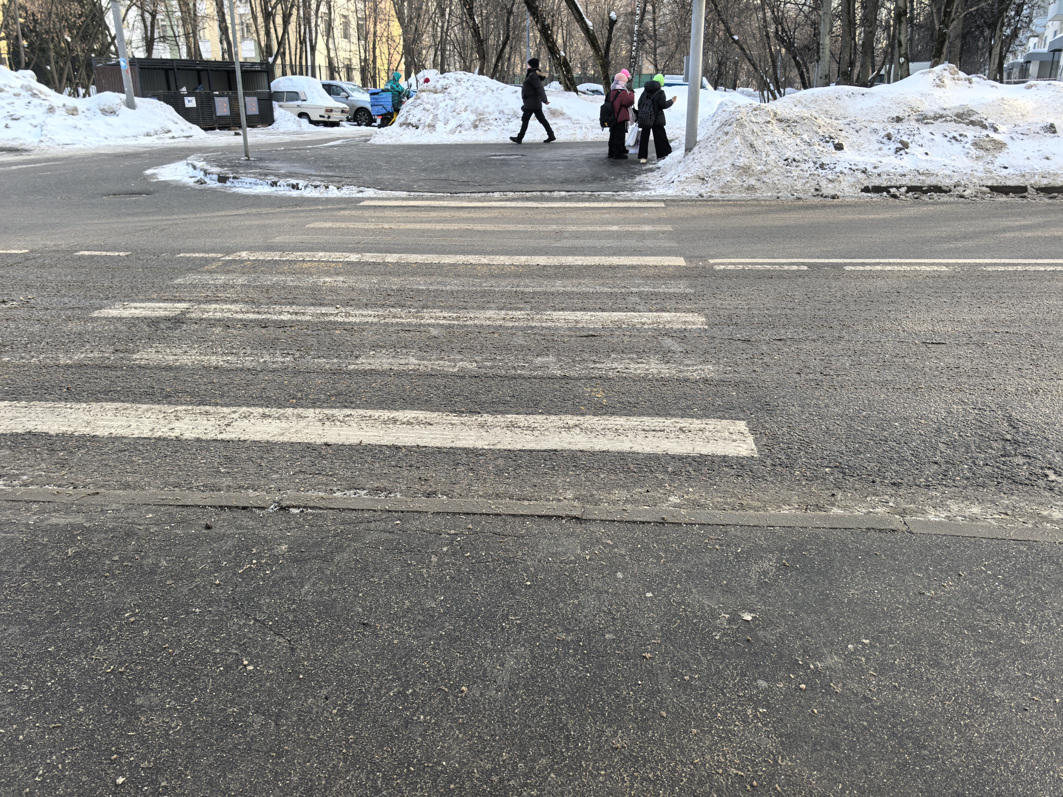 Участок проезжей части с пешеходным переходом (зебра), видны пешеходы и припаркованные автомобили на обочине в зимний период.
