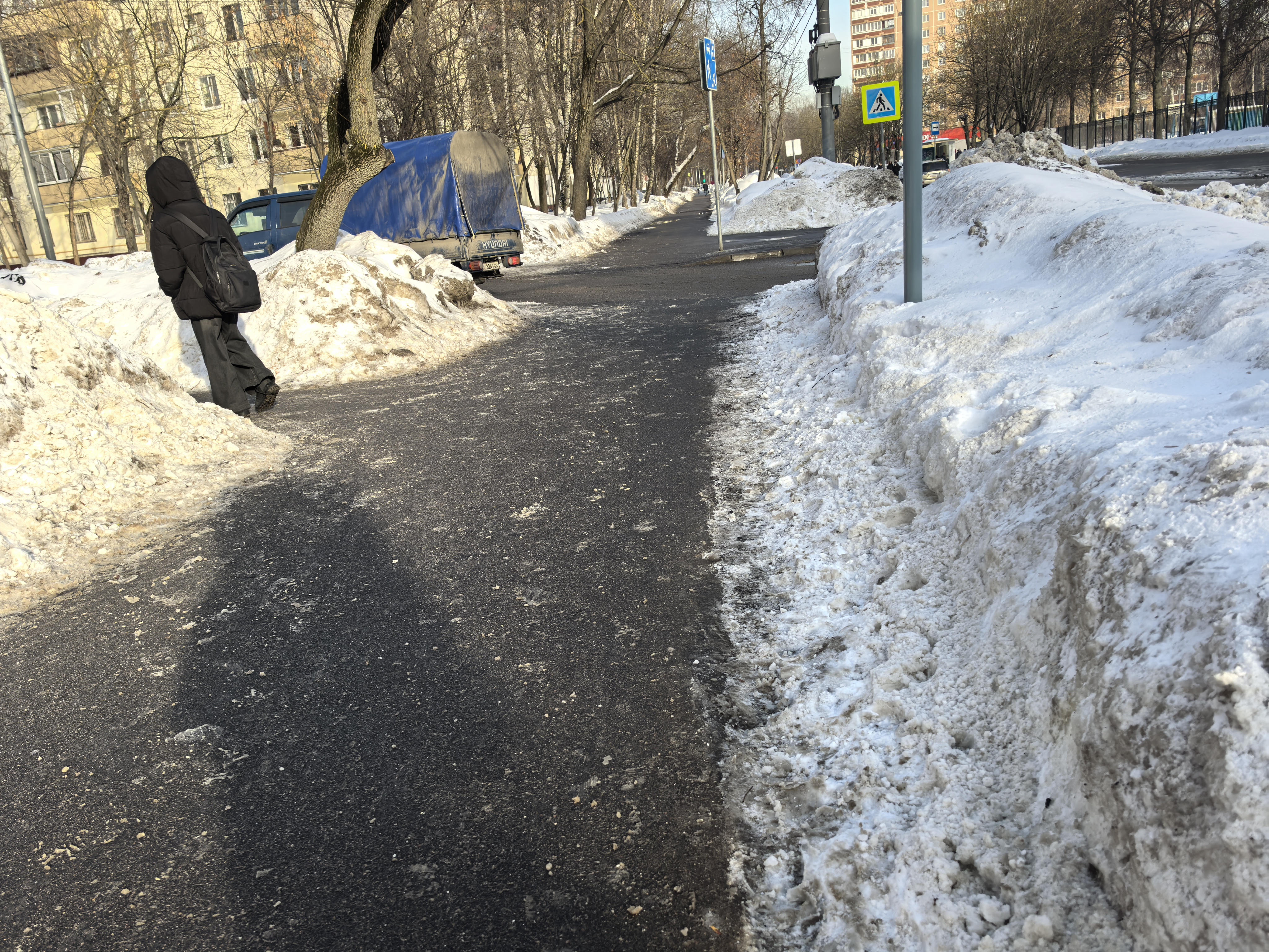 Участок дороги с пешеходным переходом, видимым знаком и разметкой, окружен высоким снегом.