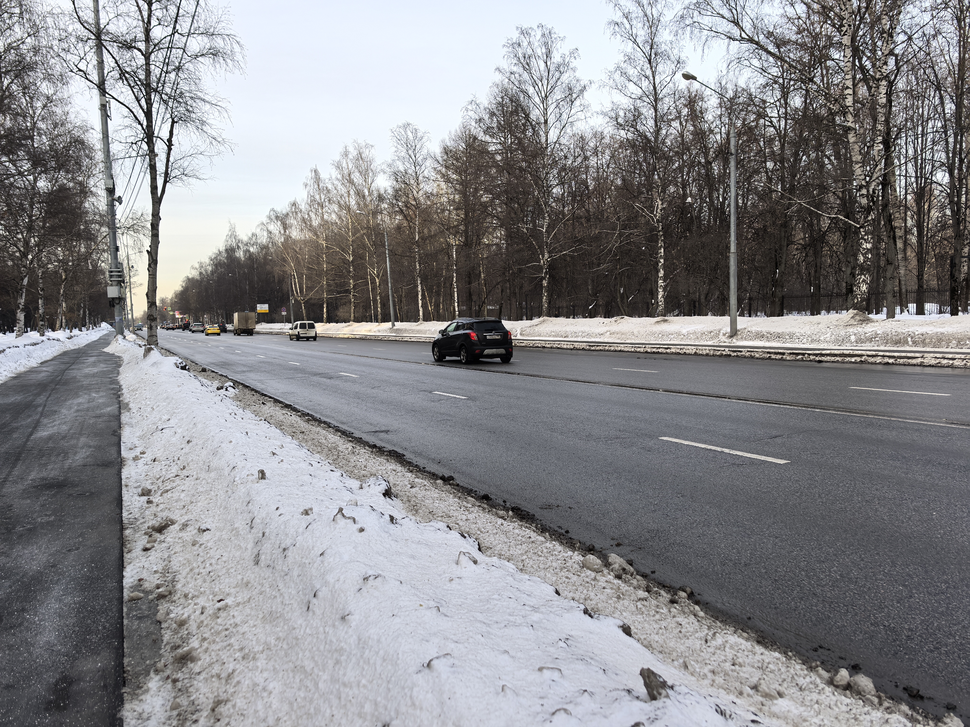 Широкая проезжая часть с разделительной полосой и тротуаром, пешеходный переход в зоне видимости отсутствует.