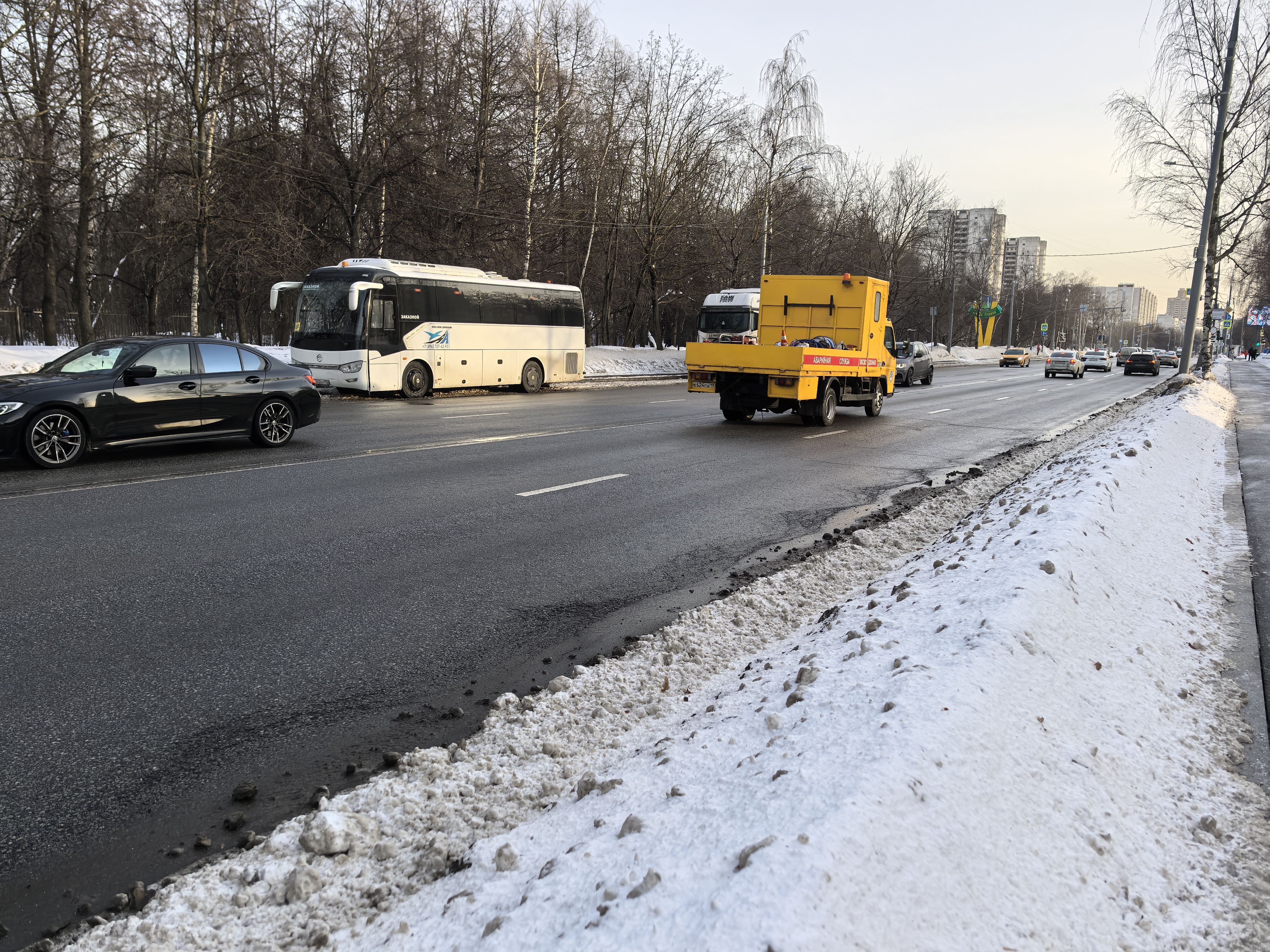 Широкая городская магистраль без пешеходного перехода в кадре. Справа виден тротуар, отделенный от дороги снежным валом. На проезжей части движется транспорт.