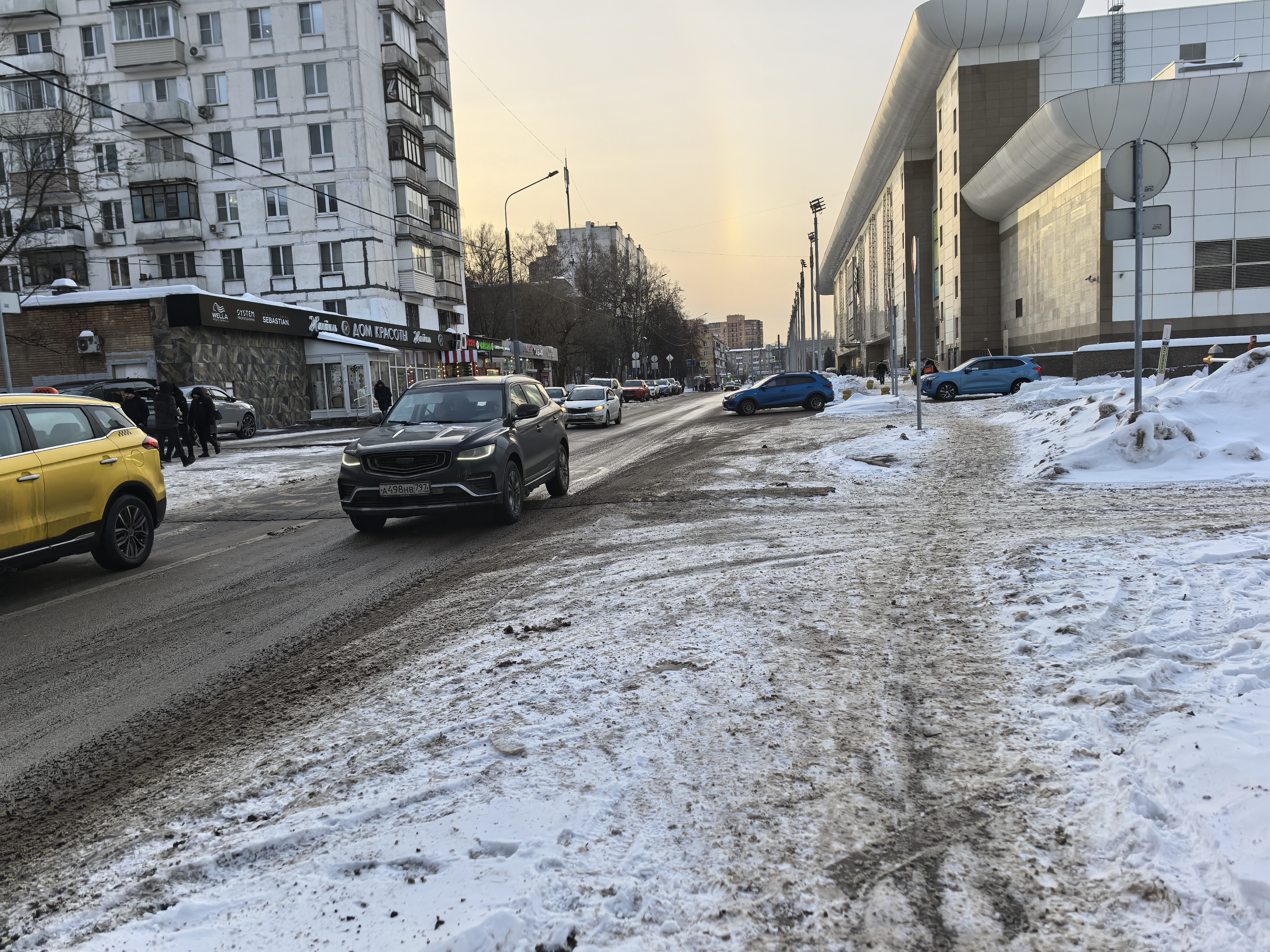 Городская улица с проезжей частью, на которой отсутствуют пешеходные переходы. Дорога покрыта снегом и слякотью, тротуары также засыпаны снегом и не убраны.